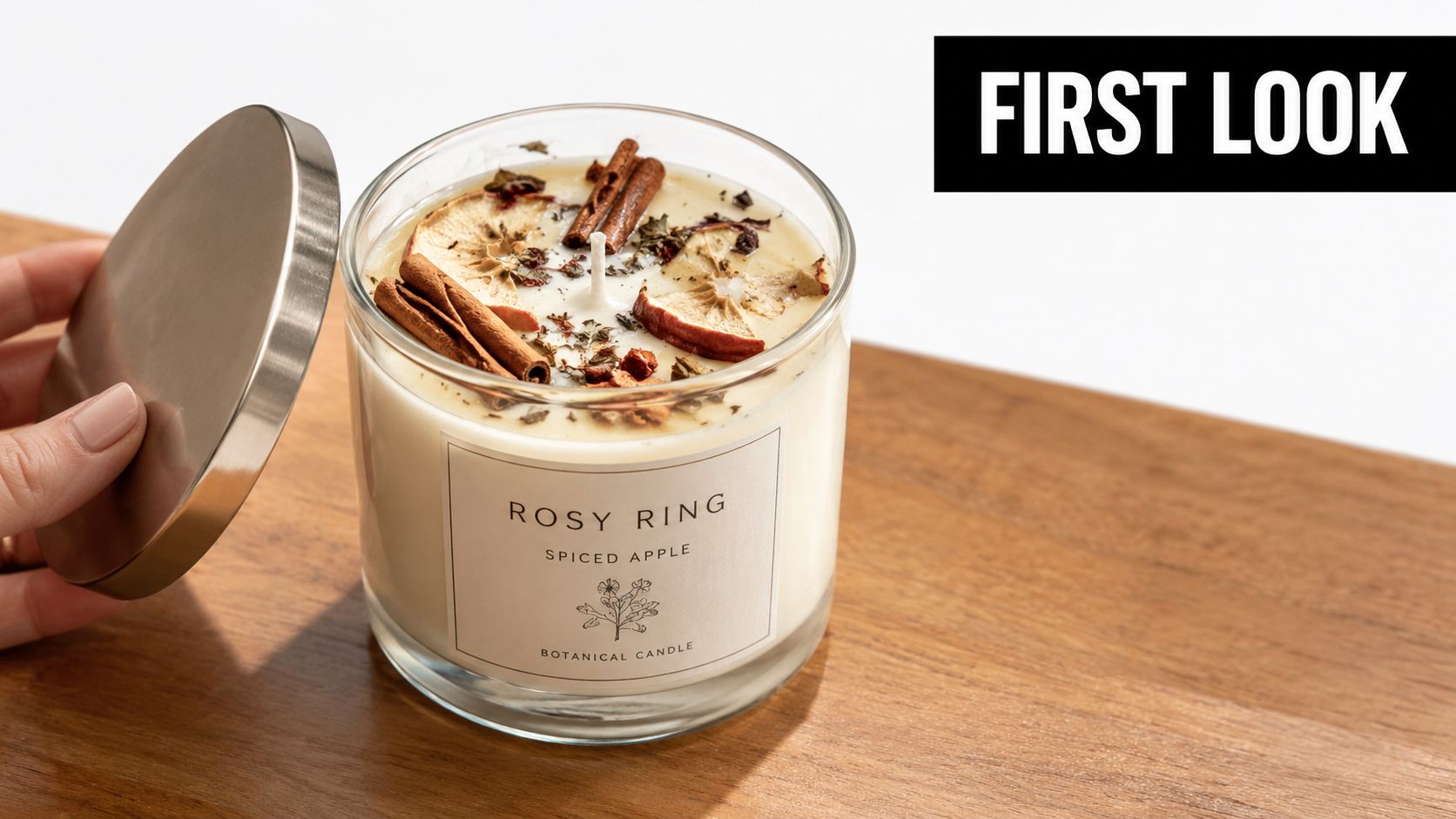 A Rosy Ring Spiced Apple botanical candle sitting on a wooden surface with its metal lid held nearby.