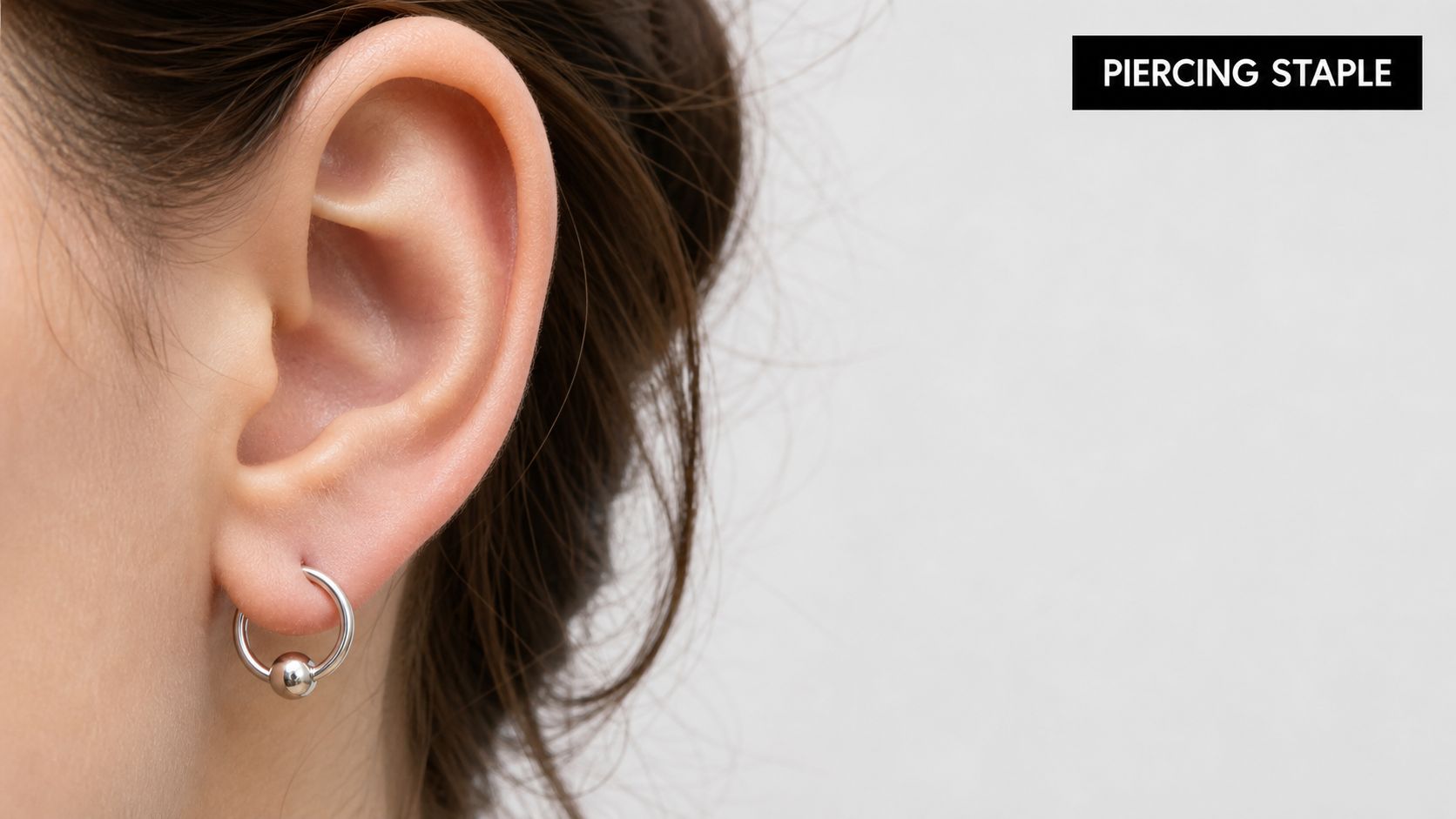 A close-up view of a human ear wearing a silver captive bead ring earring.