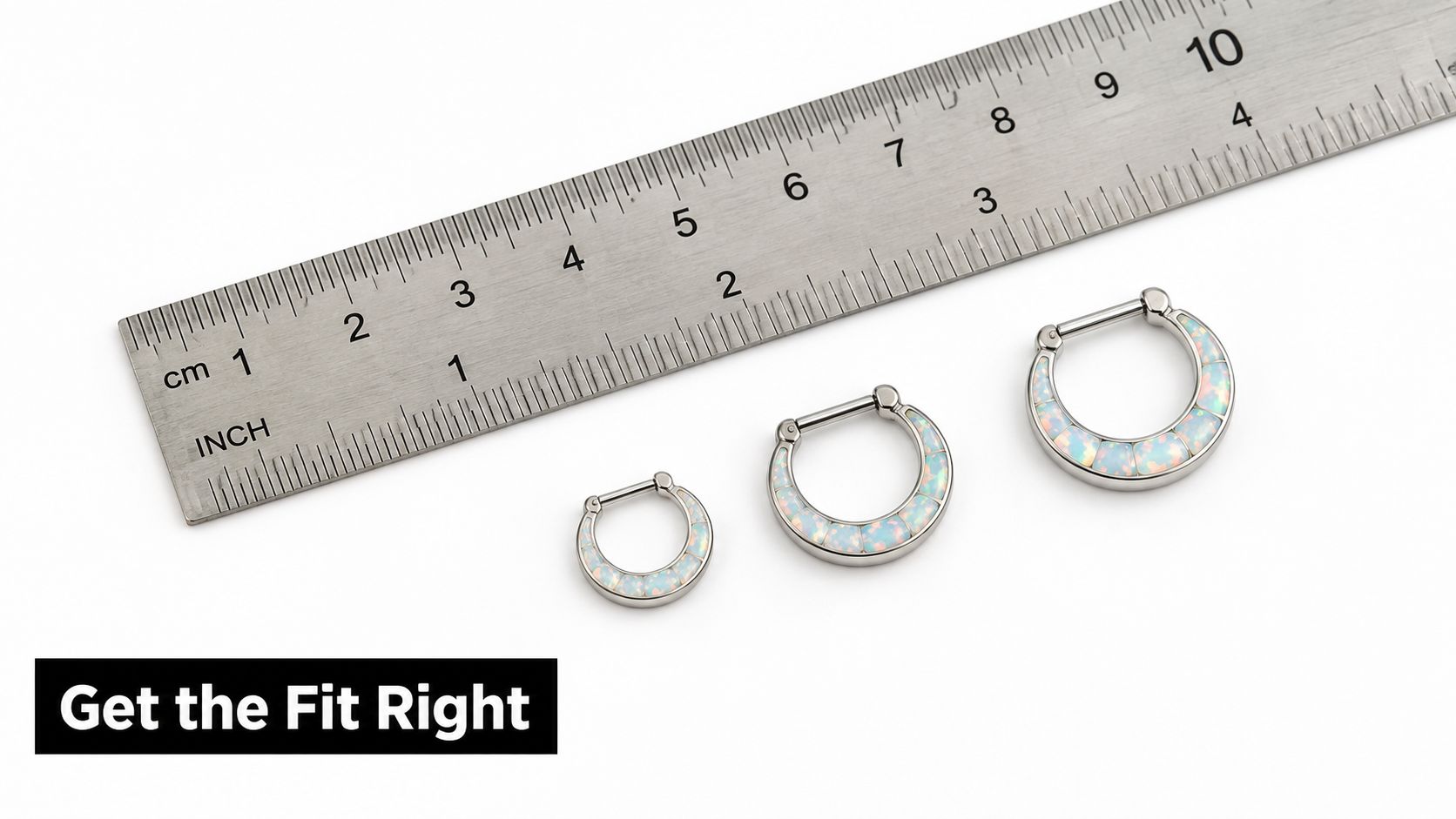 Three opal septum clicker rings in different sizes lined up next to a metal measuring ruler.