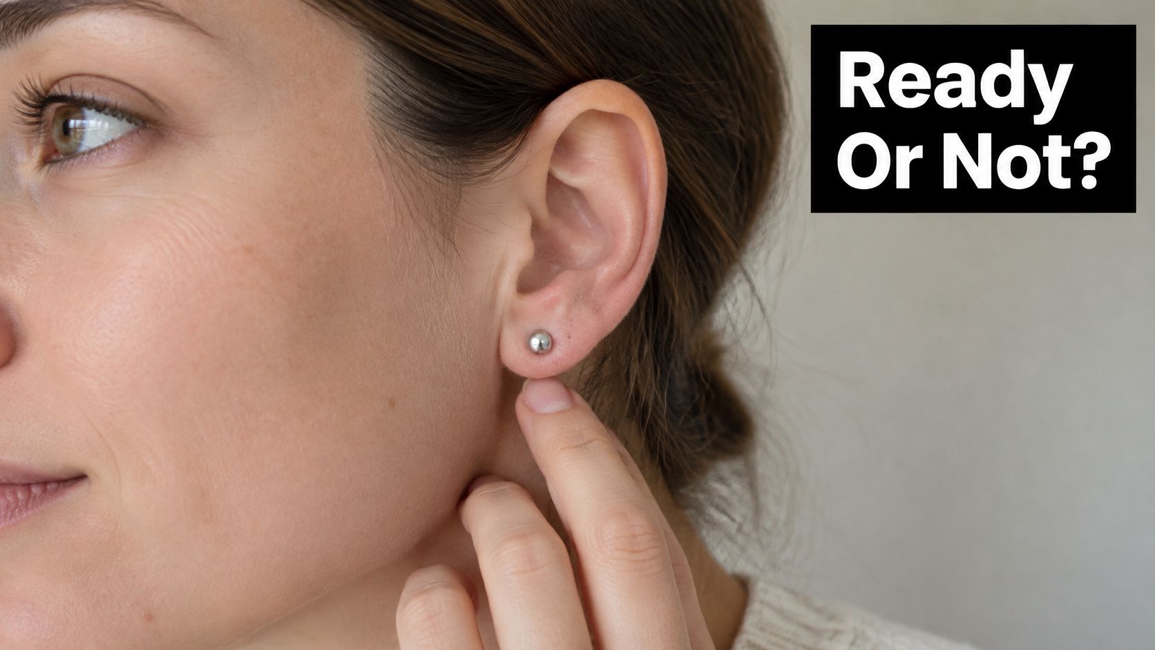 A woman's ear with a small silver stud earring as she gently touches her earlobe.