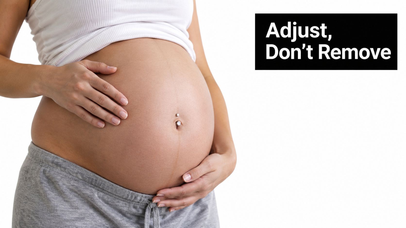 A close-up view of a pregnant woman's belly with a navel piercing, focusing on her midsection.