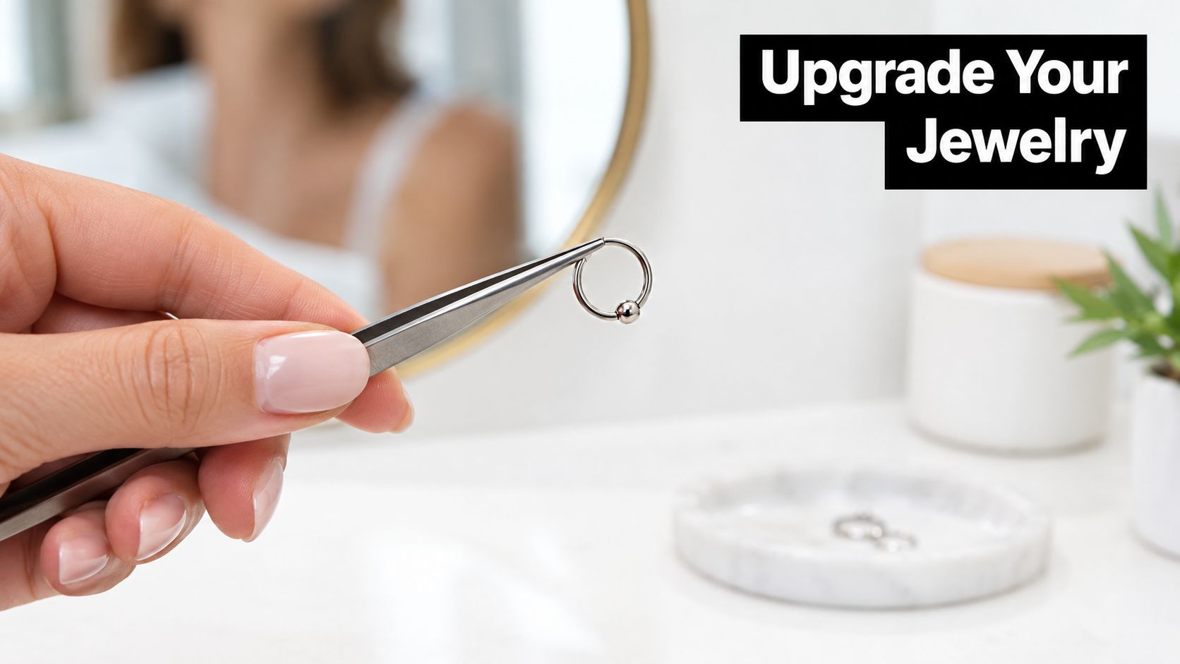 A hand holding a metallic circular nose ring with a bead using silver tweezers near a vanity.