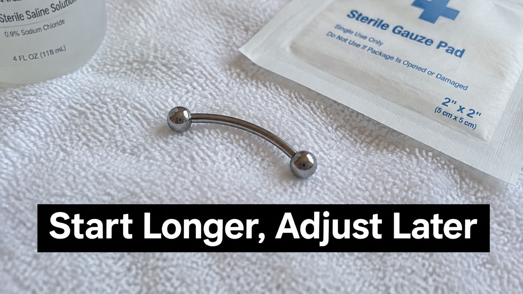 A curved barbell piercing jewelry rests on a white towel next to sterile saline and gauze.