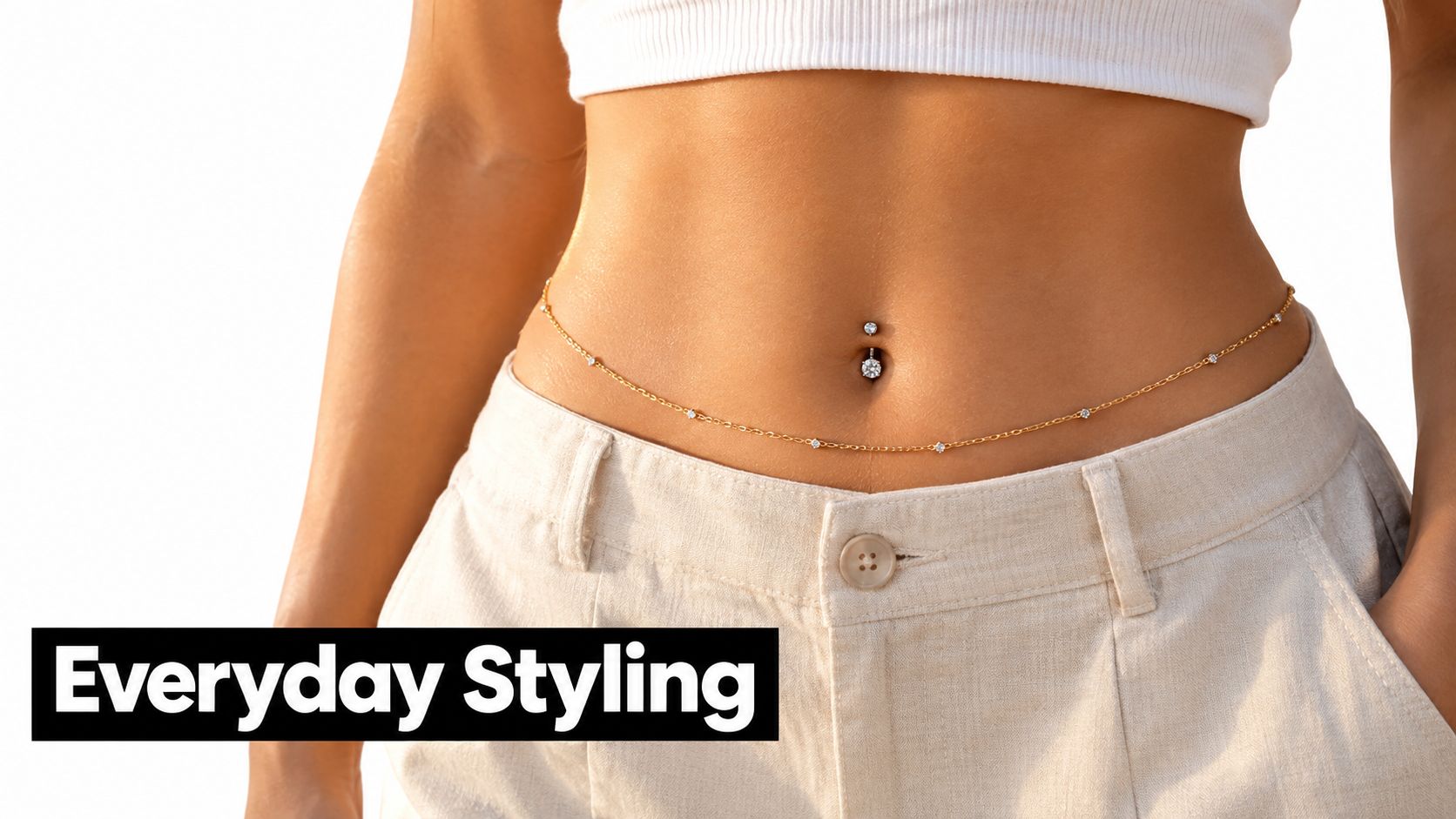 A close-up view of a woman wearing a delicate gold waist chain over her belly button piercing.