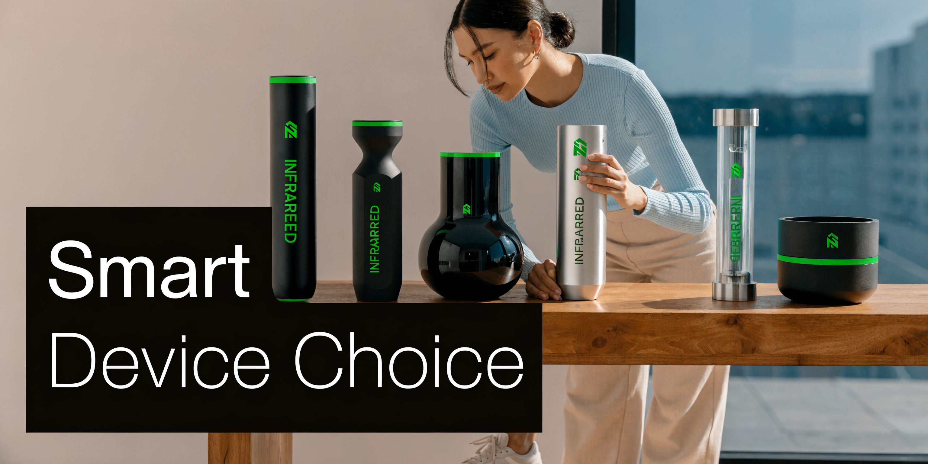 A young woman displaying various modern infrared light therapy devices on a wooden table in a bright room.