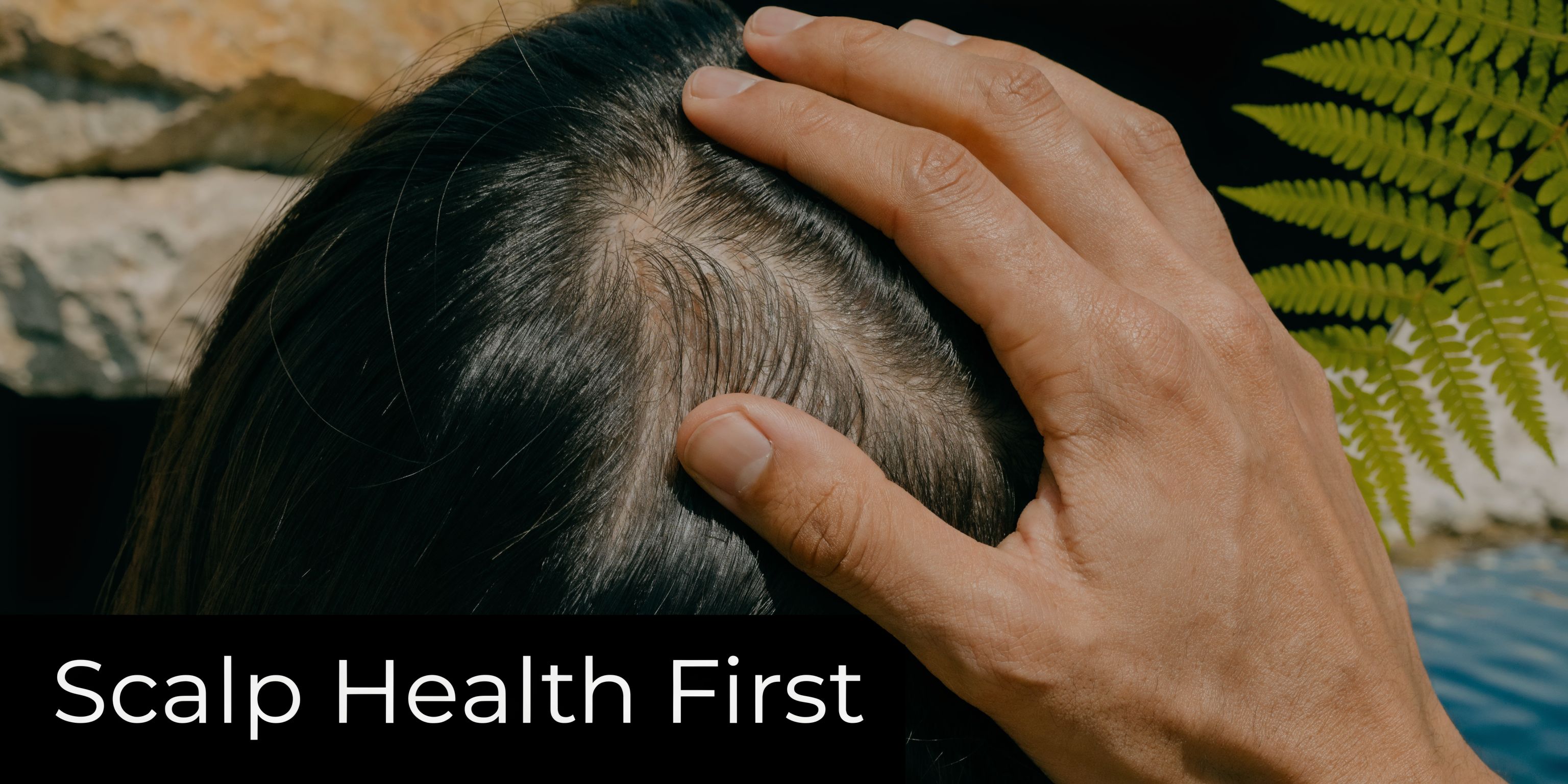 A close-up view of a person gently touching their dark hair and healthy-looking scalp outdoors.