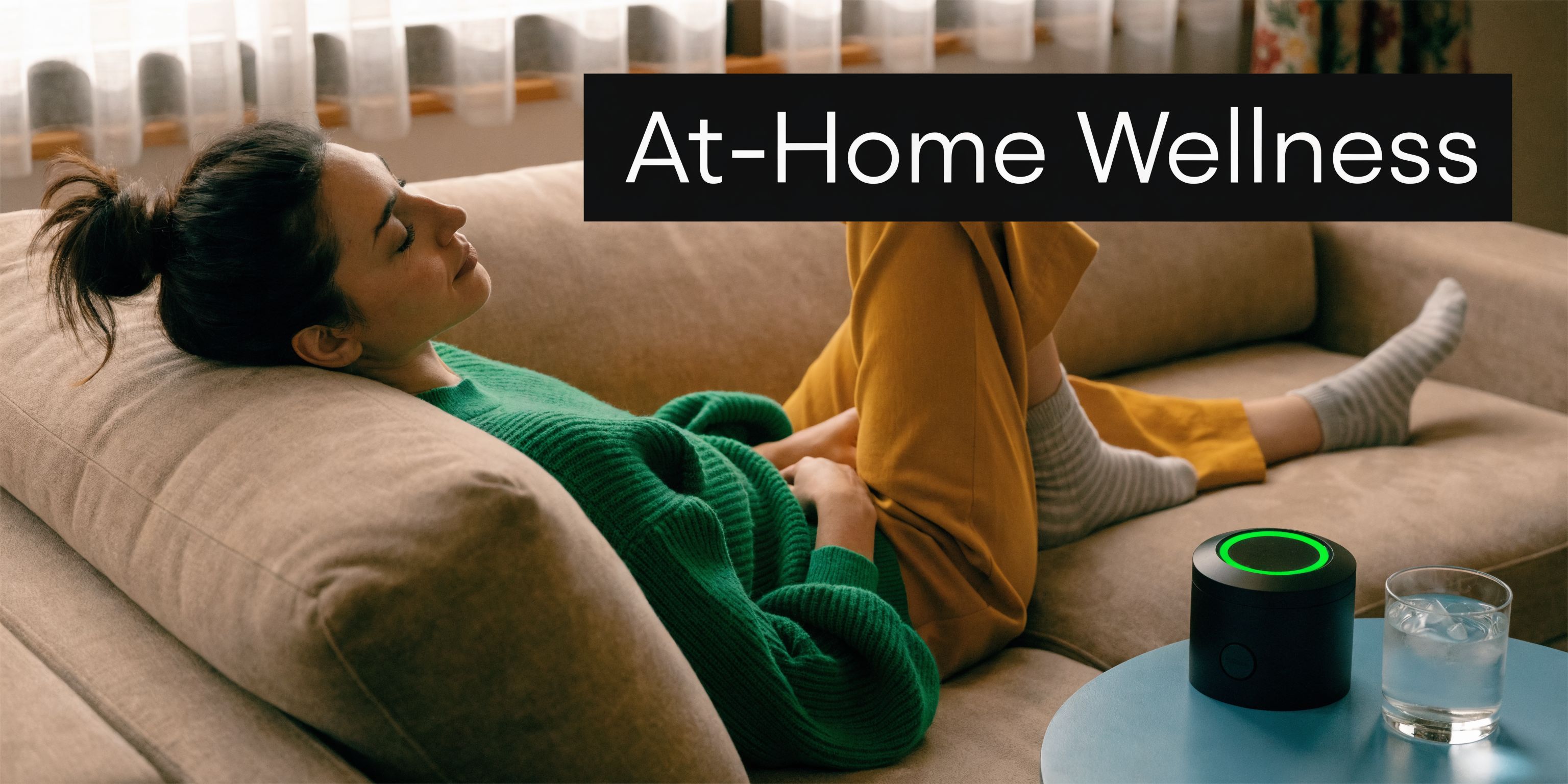 A relaxed woman lounging on a couch next to an infrared light therapy device and water.
