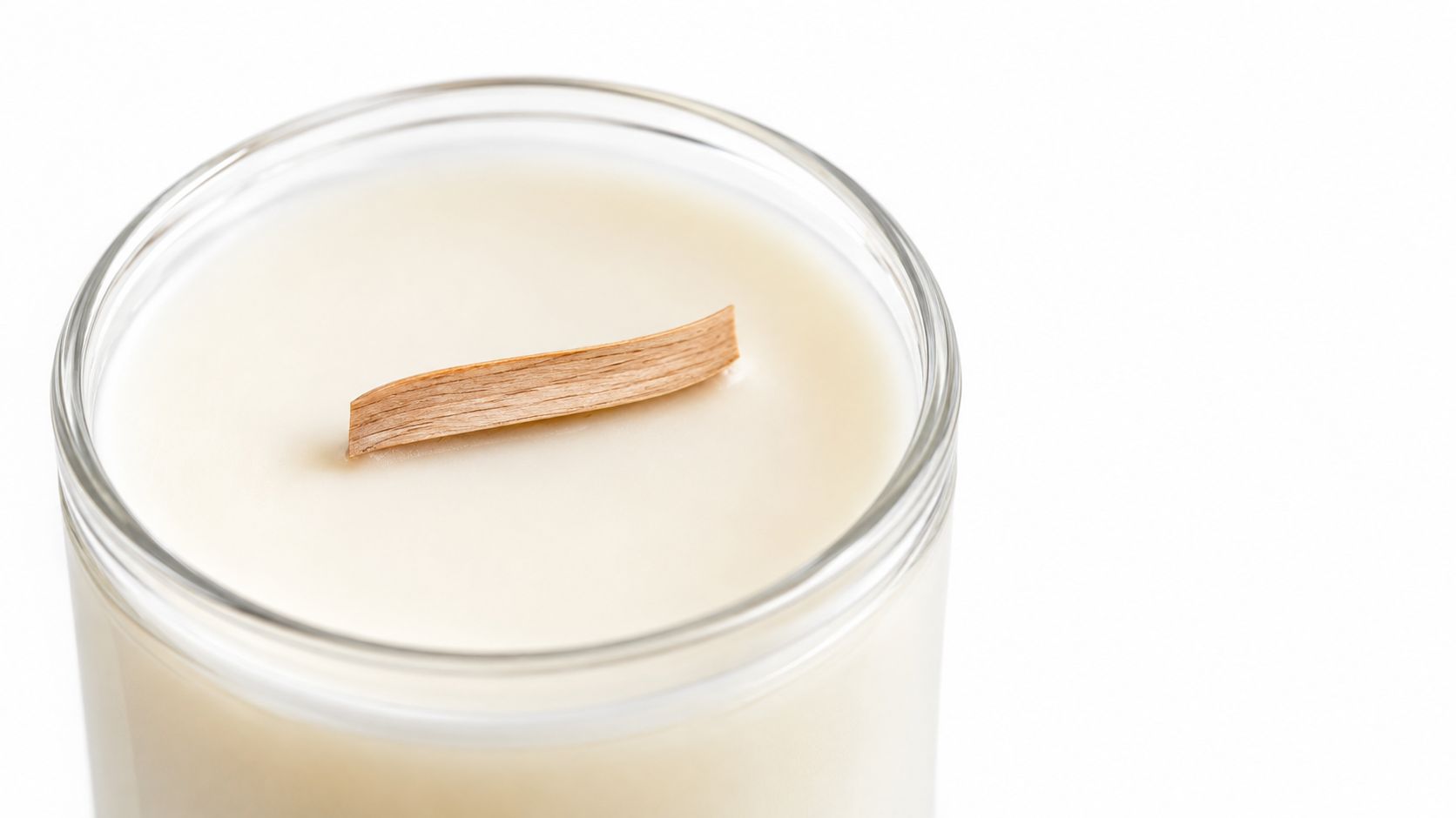 A close-up view of an unlit scented candle in a glass jar featuring a thin wooden wick.