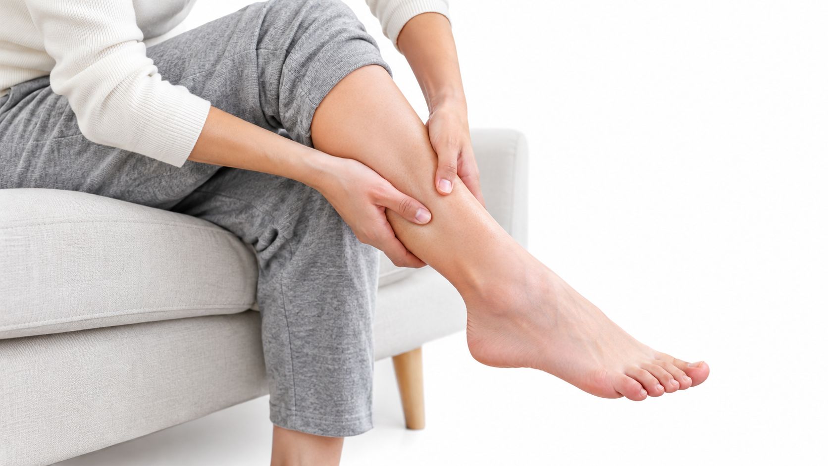 Une personne assise sur un canapé massant doucement son mollet pour soulager une douleur à la jambe.