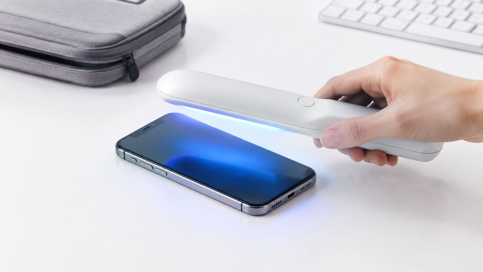 A hand holding a white handheld UV sterilizer wand disinfecting the surface of a modern smartphone.