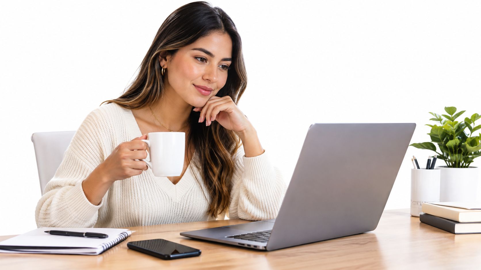 A woman smiling while looking at her laptop screen and holding a white coffee mug at home.