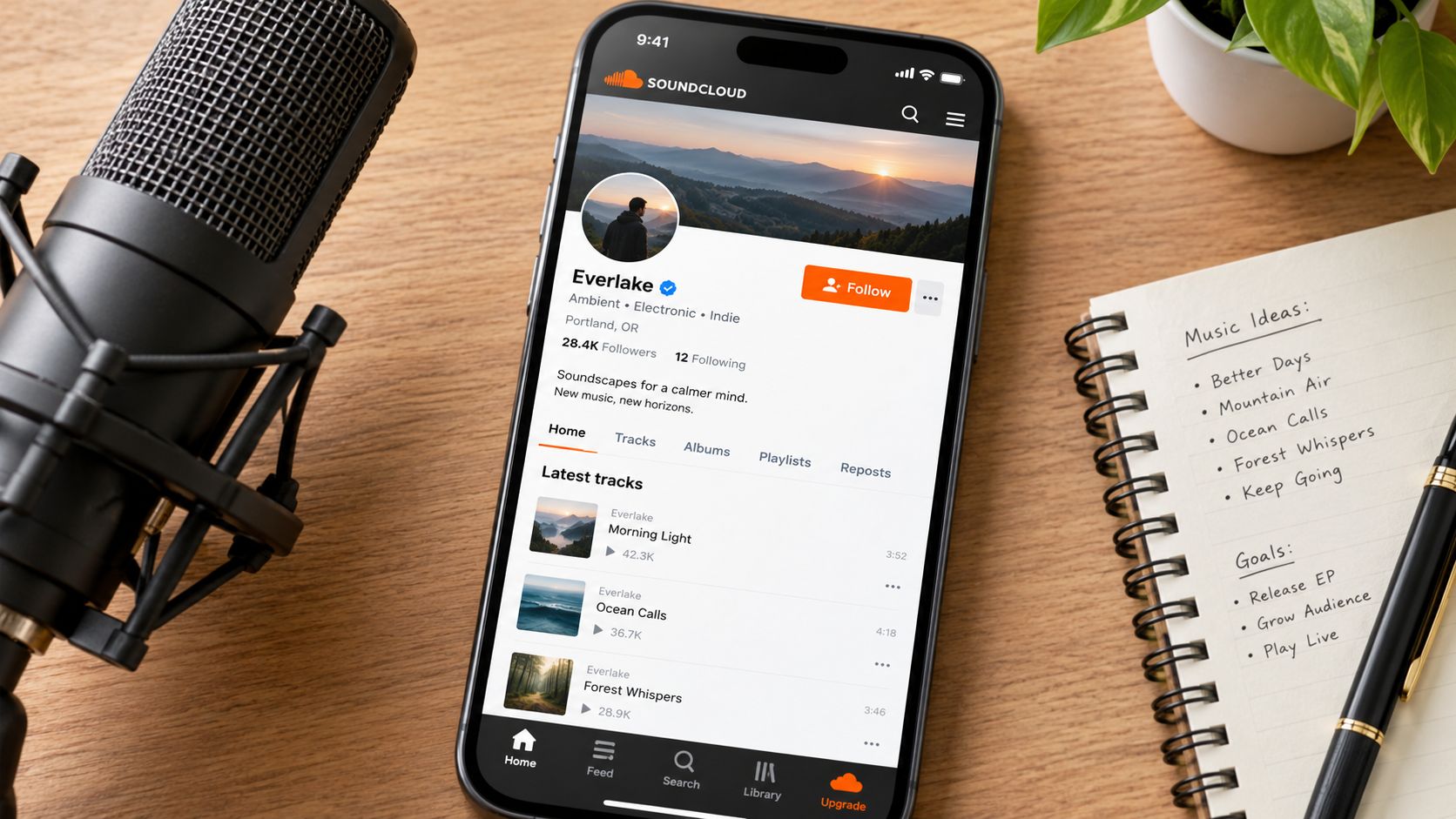 A smartphone displaying a music profile on SoundCloud beside a microphone and a handwritten music planner.