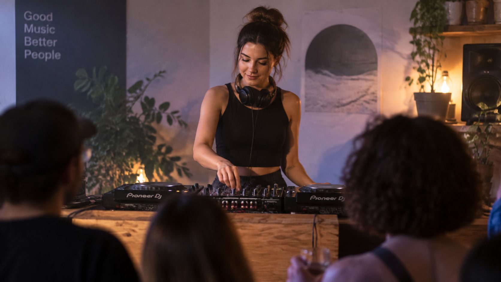 A female DJ smiling while performing a music set on Pioneer DJ equipment at a lively venue.