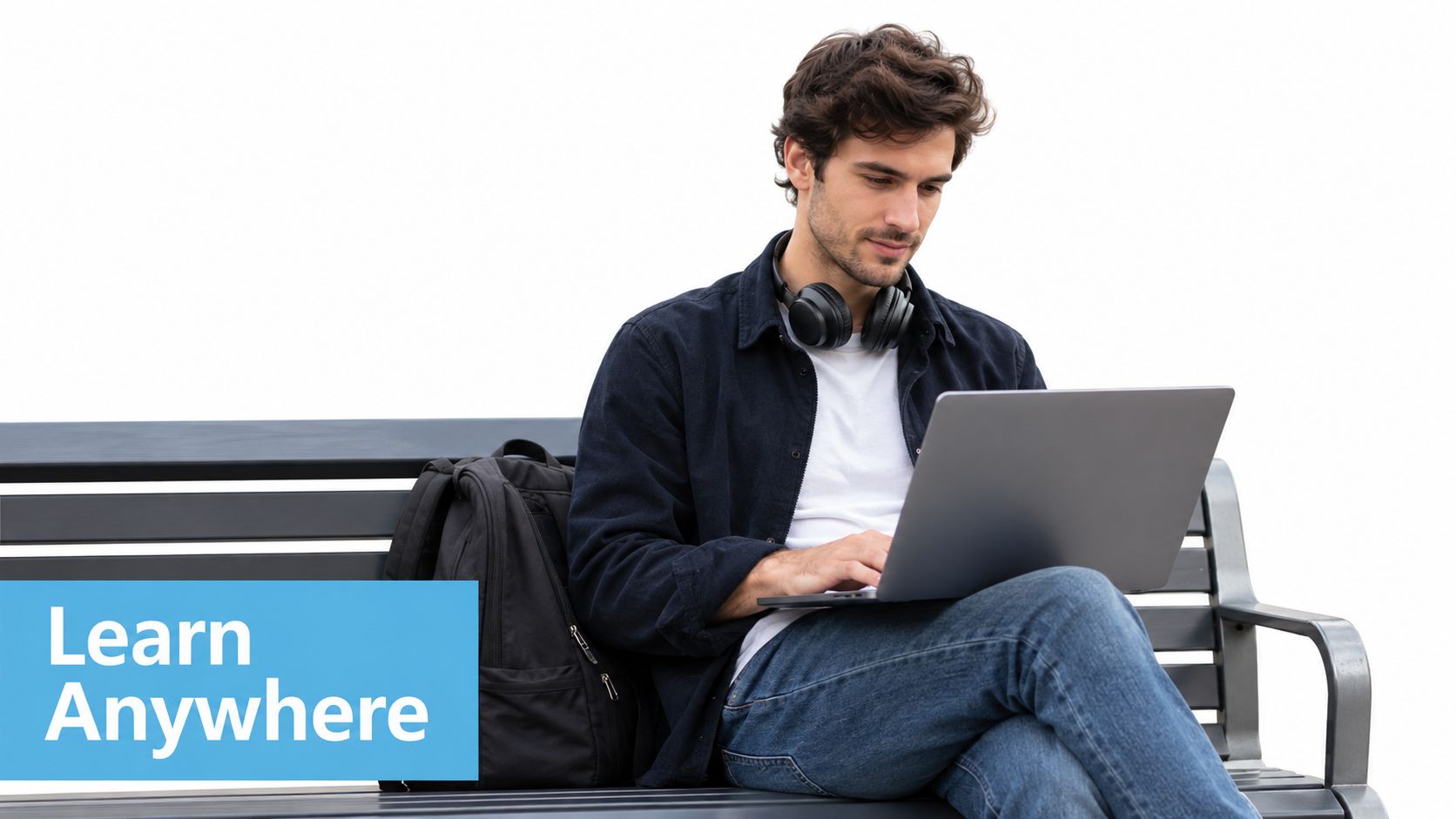 A young man sitting on a park bench while working on his laptop with a backpack nearby.