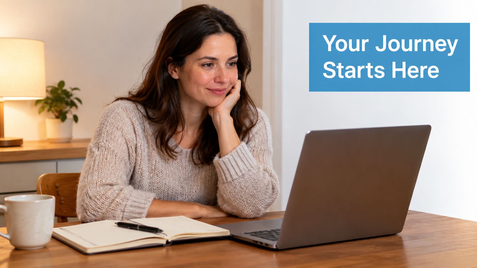 A smiling woman sits at a desk with a laptop, notebook, and coffee, focusing on her studies.