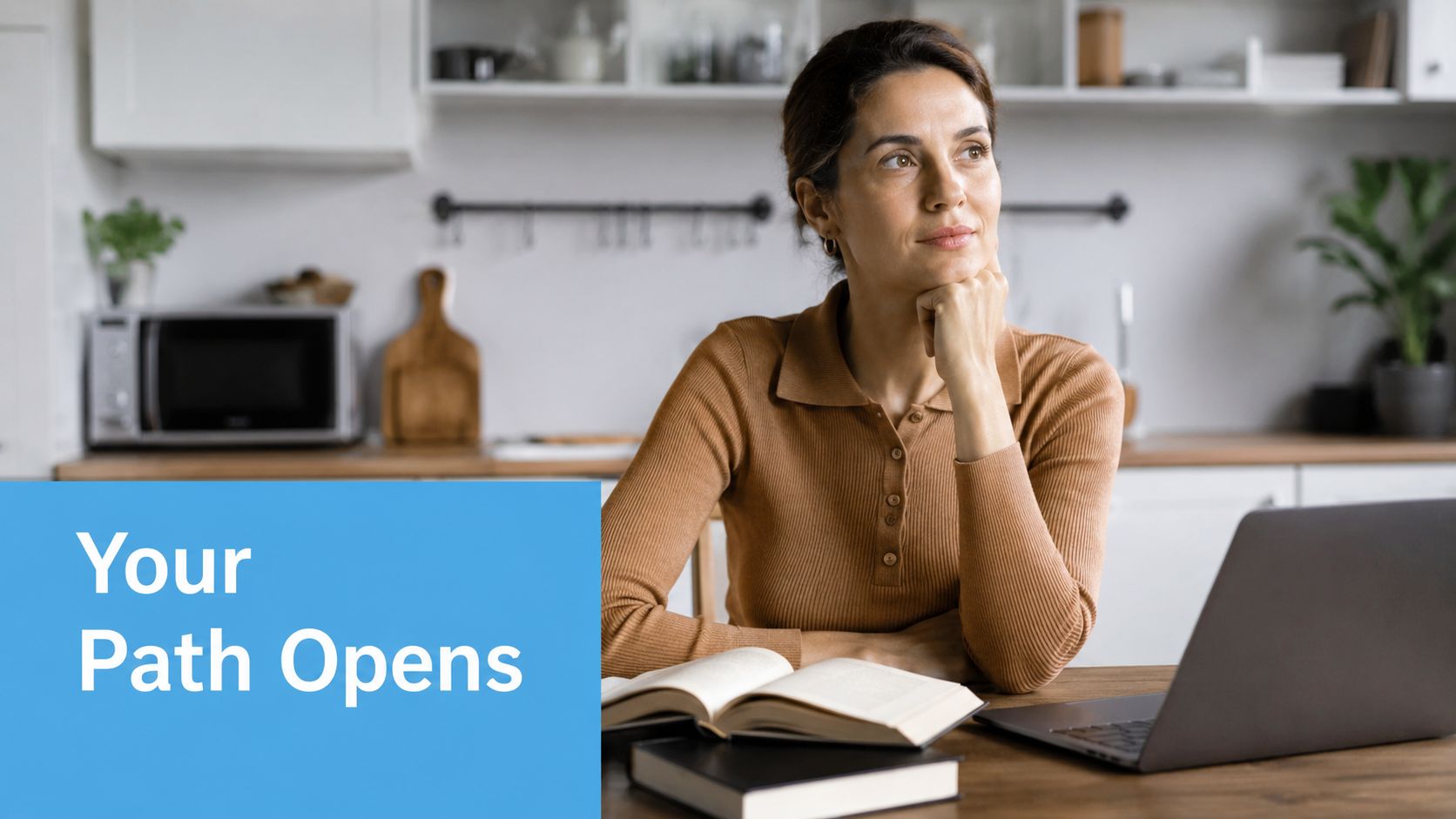 A woman in a brown sweater sitting at a desk with an open book and a laptop.