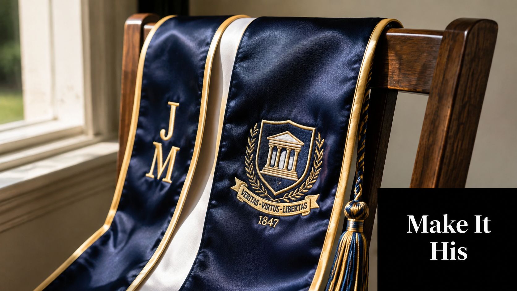 A graduation stole with initials J M and university emblem draped over a wooden chair.