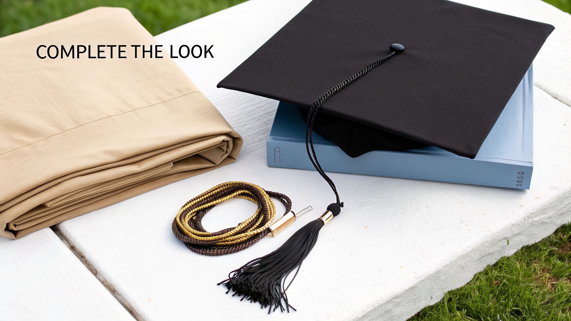 A graduation setup with a folded beige gown, black cap, tassel, and gold academic cord.
