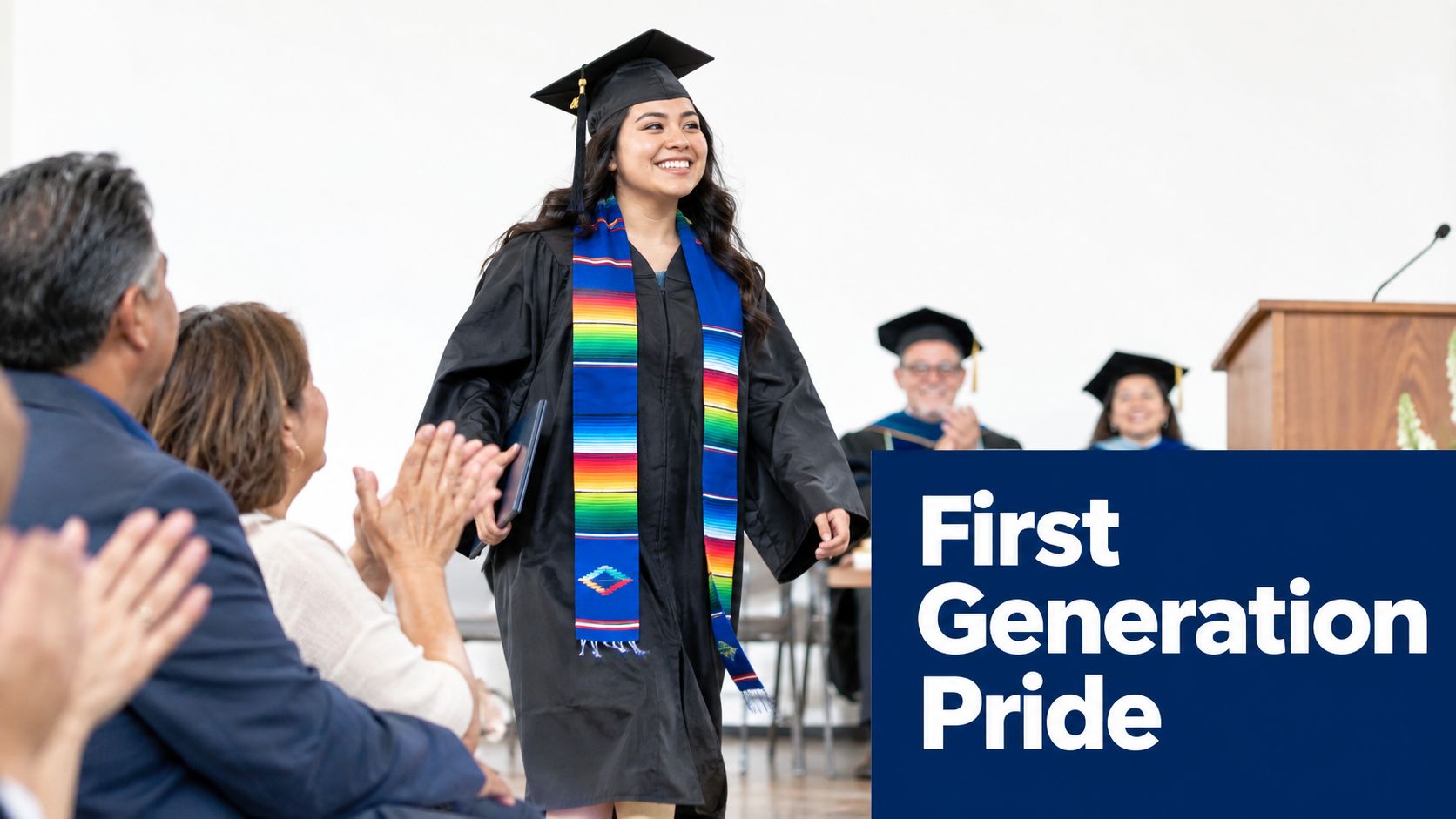 A happy college graduate wearing a colorful Mexican serape stole walks across the stage while people applaud.