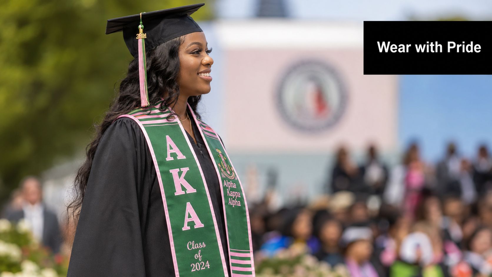 A female graduate wearing a black graduation cap and an Alpha Kappa Alpha sash with pride.