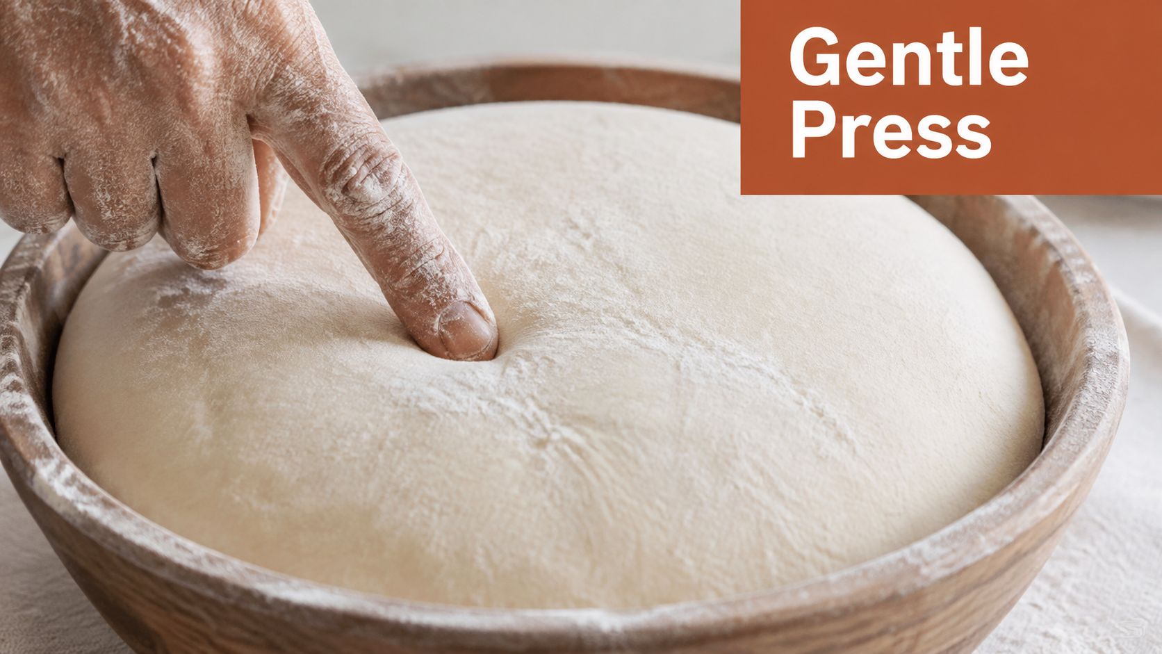 A baker's finger gently pressing into a mound of proofing dough in a wooden bowl.