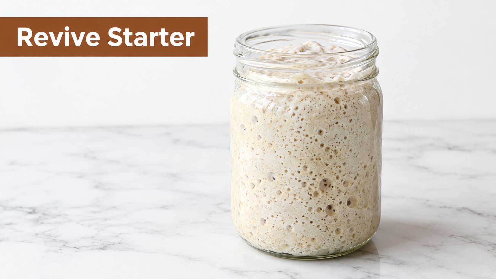 A close-up view of an active, bubbly sourdough starter inside a clear glass jar on a marble surface.