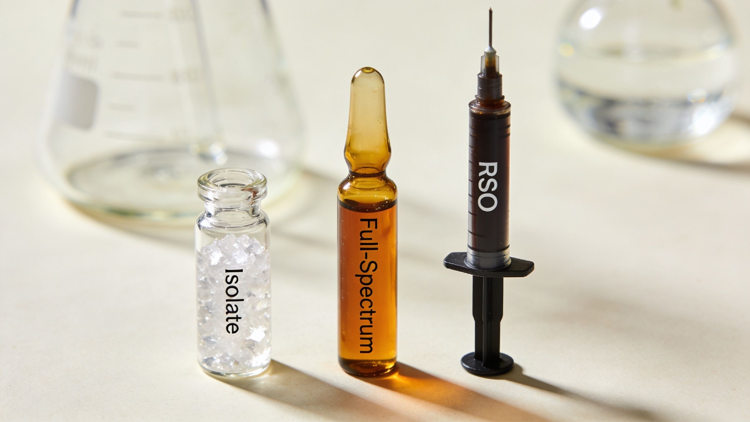 A laboratory display featuring clear isolate crystals, a full-spectrum amber vial, and an RSO syringe for cannabis products.