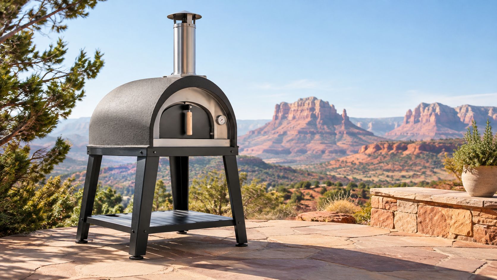 A black outdoor pizza oven stands on a patio with a scenic mountain landscape in the background.