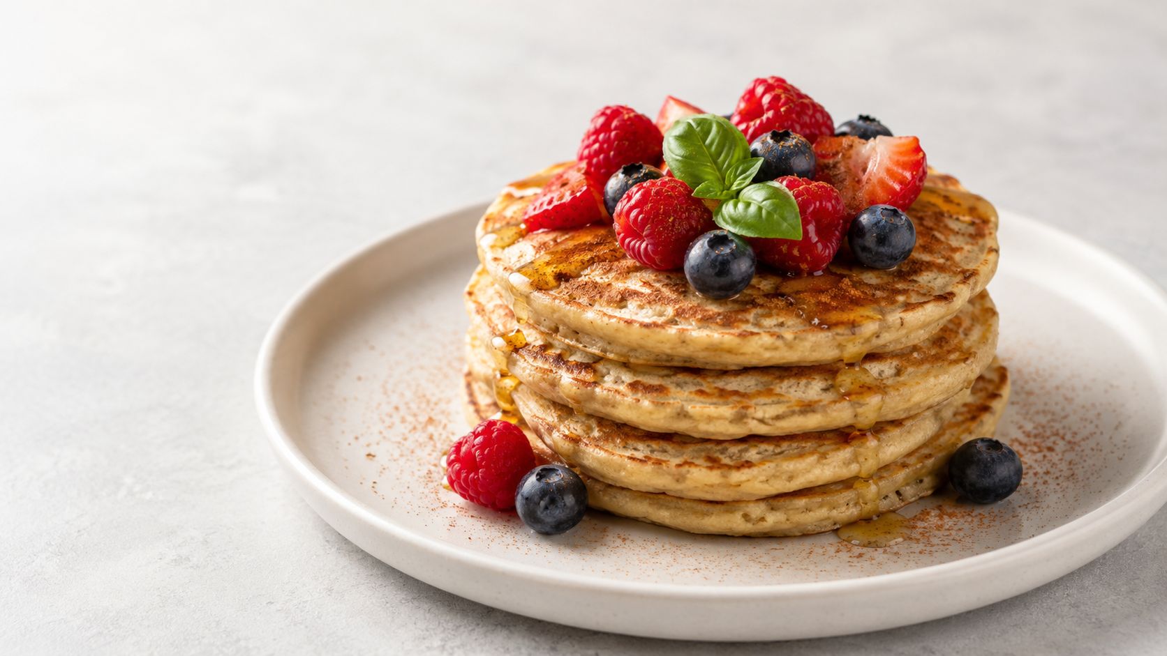 A delicious stack of fluffy pancakes topped with fresh berries, maple syrup, and green basil leaves.