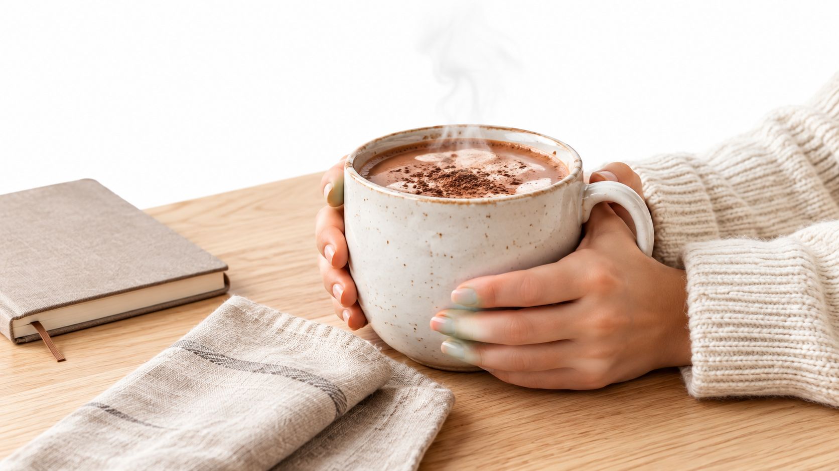 A person in a cozy sweater holding a steaming mug of hot chocolate on a wooden table.