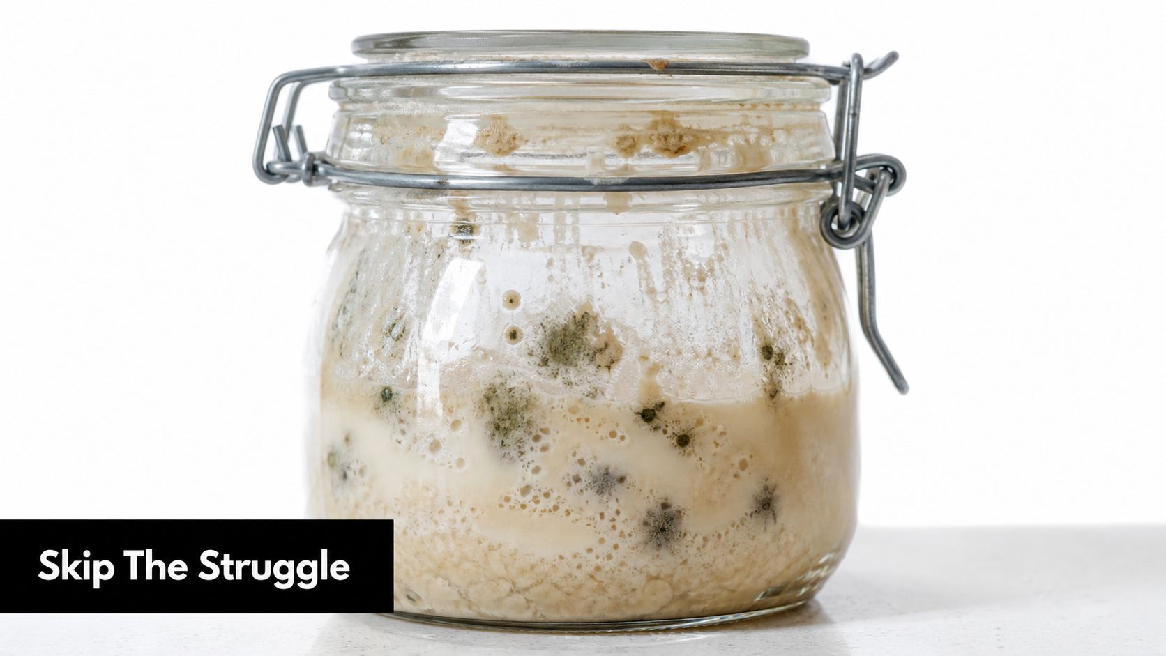 A clear glass jar filled with moldy sourdough starter sitting on a kitchen counter surface.