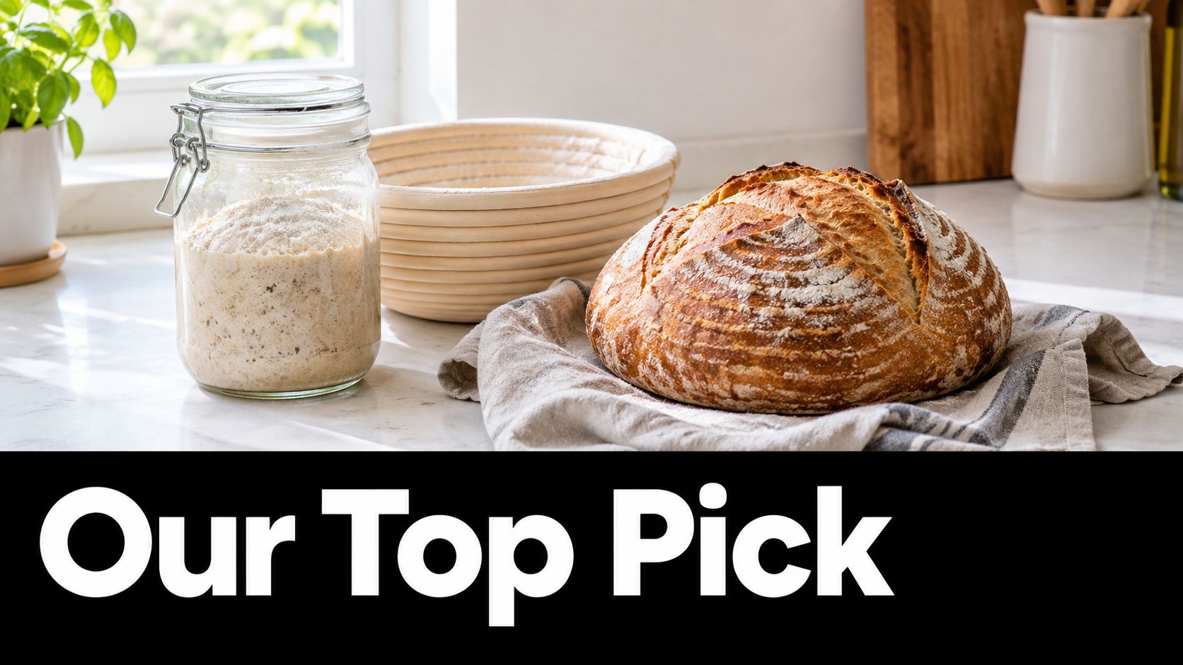 A freshly baked sourdough loaf sits next to a glass jar of active sourdough starter and a proofing basket.