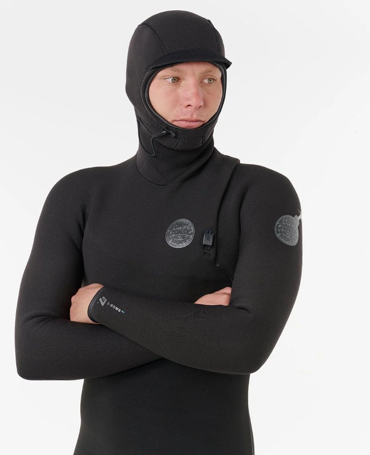 A man wearing a black hooded steamer wetsuit with crossed arms against a plain white background.