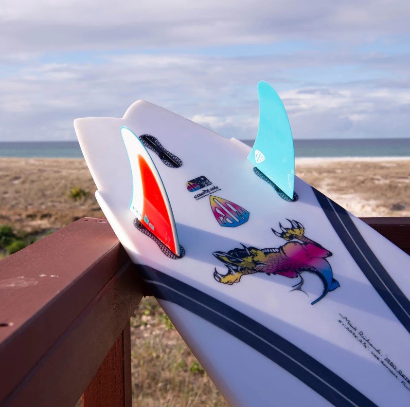 A surf board resting on a wooden railing overlooking a sandy beach and ocean under cloudy skies.