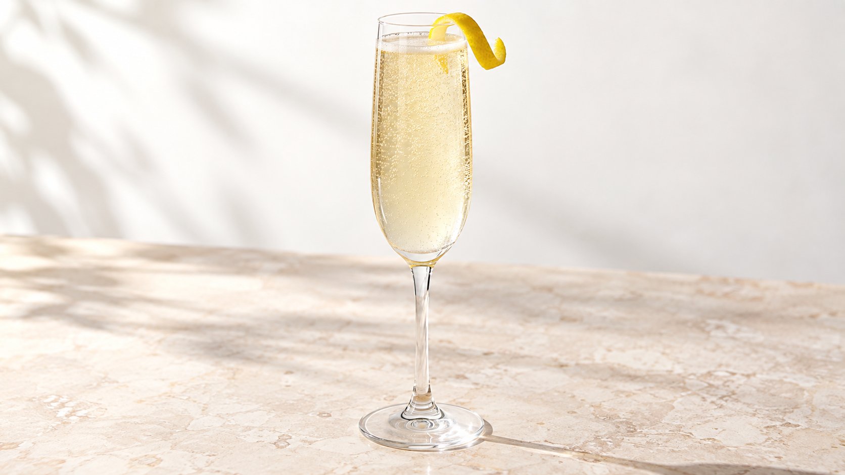 French 75 cocktail in a champagne flute with a lemon twist on a pale stone surface.