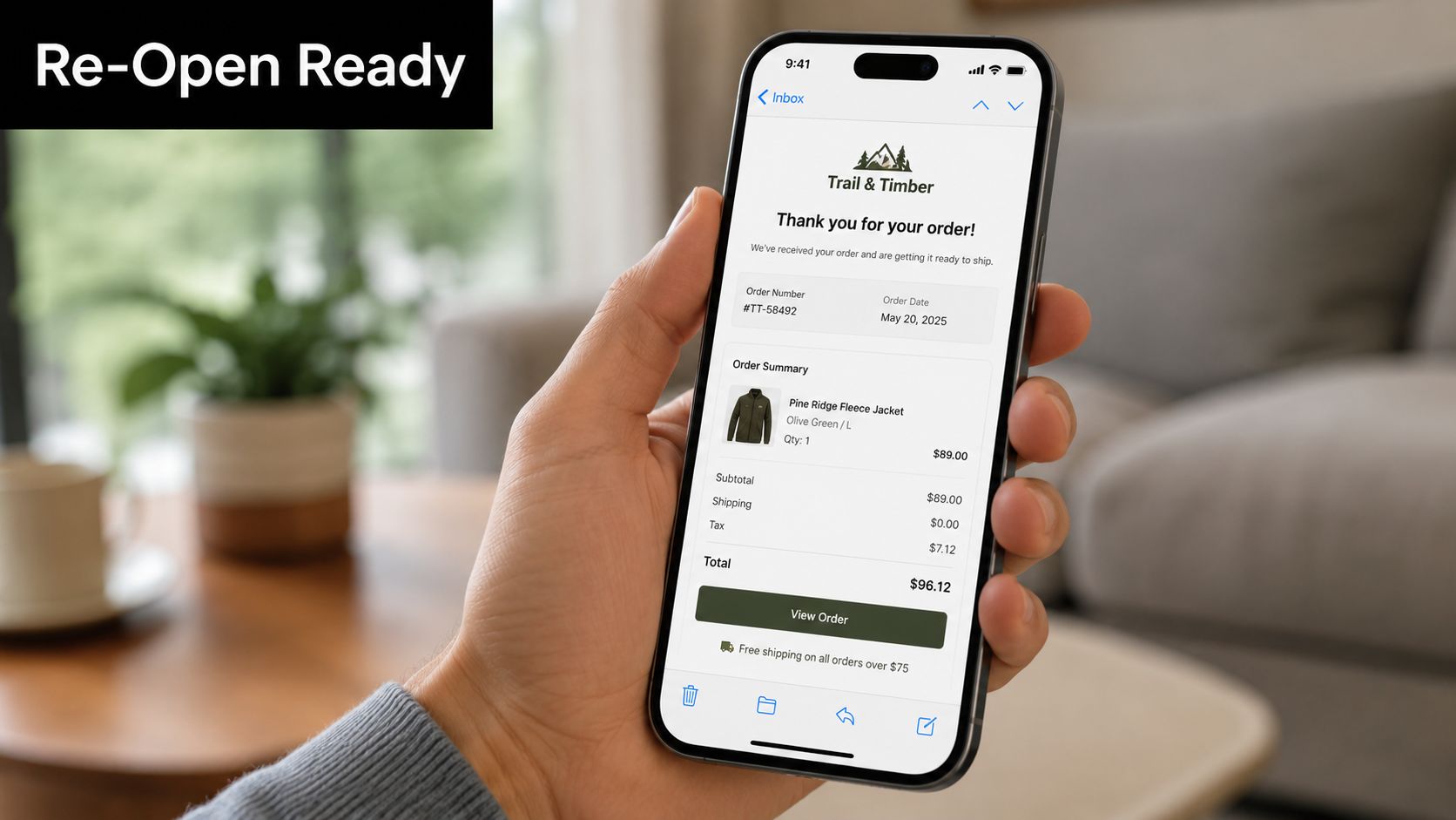 A hand holding a smartphone displaying a Trail & Timber digital order confirmation email on the screen.