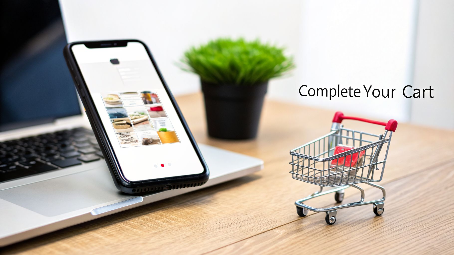A smartphone on a laptop displays products, next to a miniature shopping cart with 'Complete Your Cart' text.