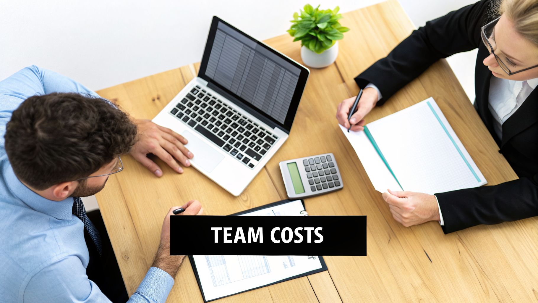 Overhead shot of two business professionals discussing team costs at a wooden table with a laptop.