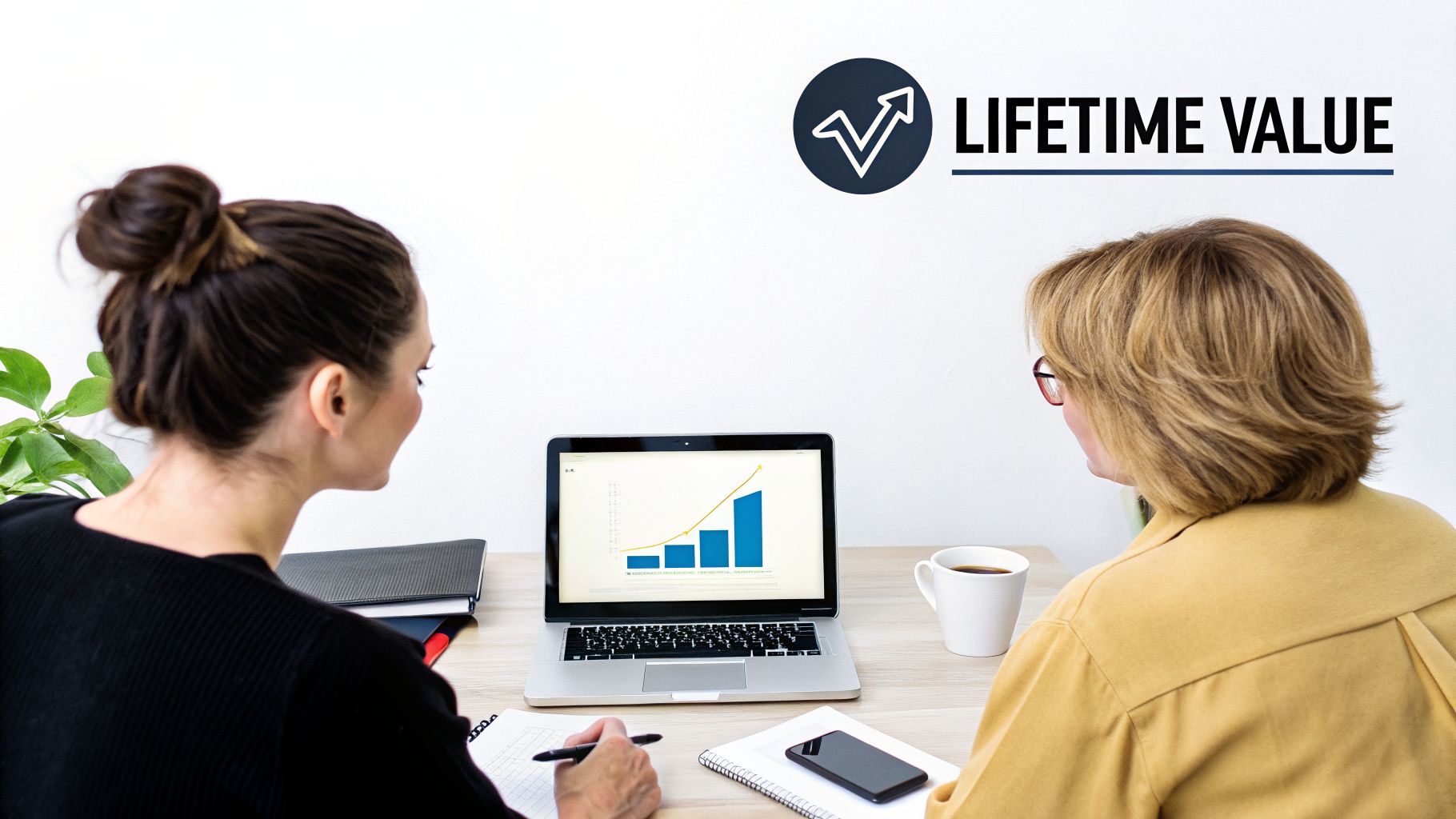 Two businesswomen analyze a growth chart on a laptop with 'LIFETIME VALUE' text, planning strategy.