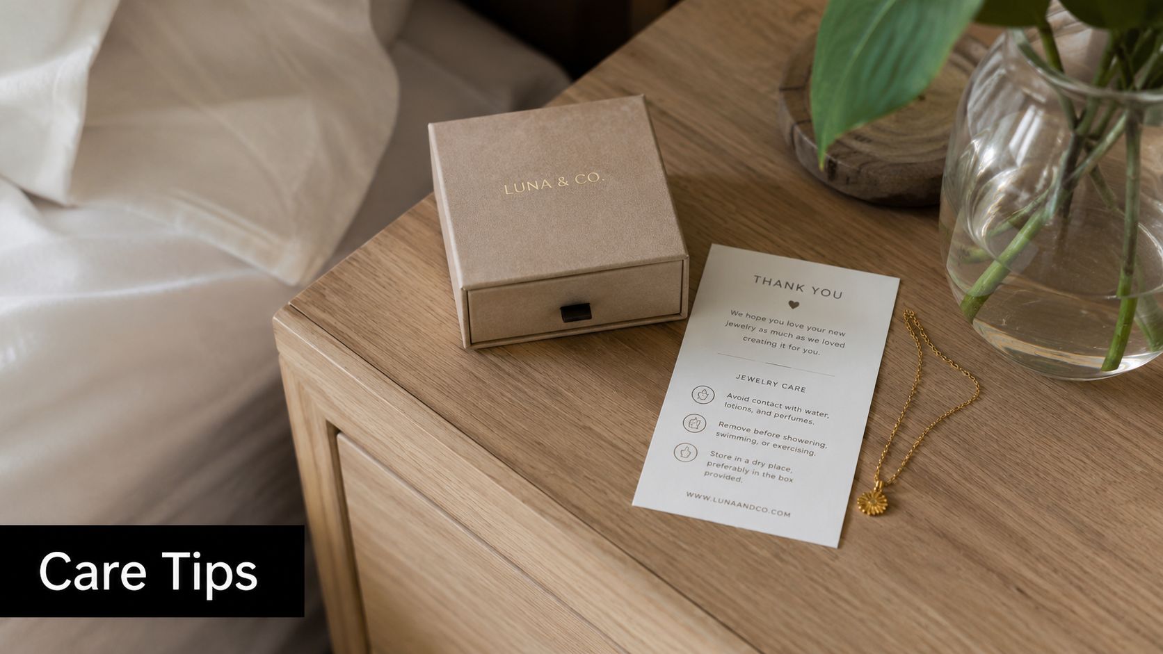 A Luna & Co jewelry box and care instructions card sitting on a wooden nightstand with a gold necklace.