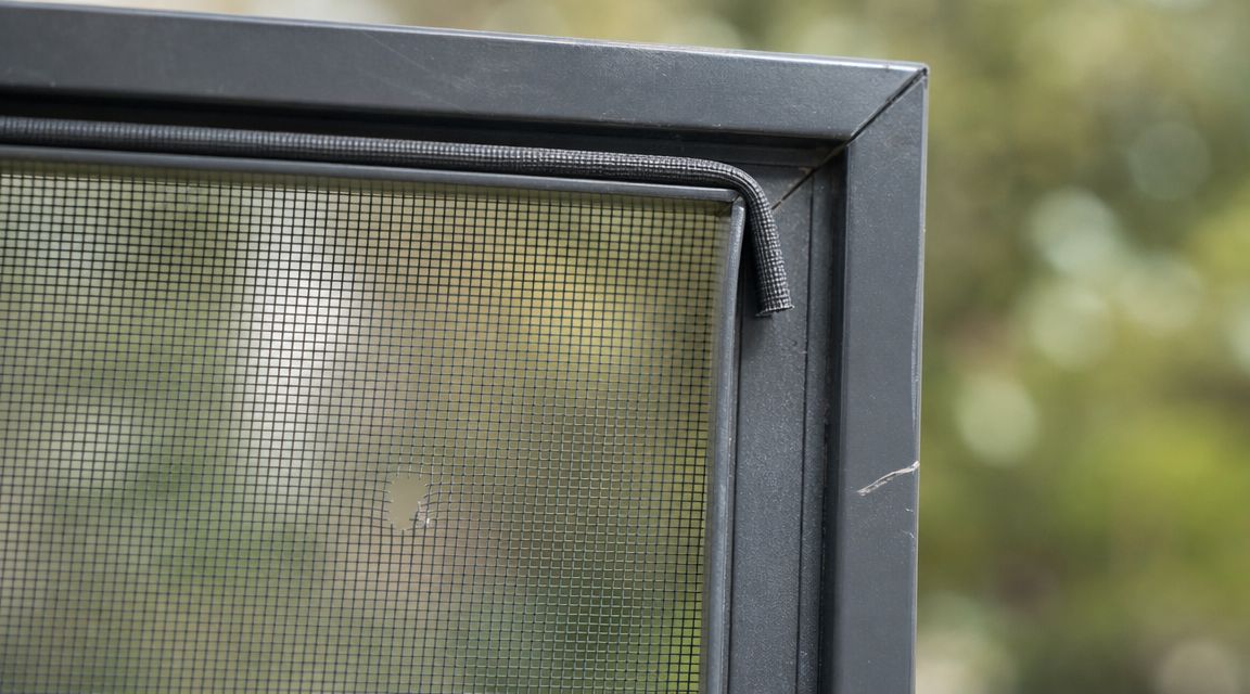 A close-up view showing a damaged window screen mesh with a tear and detached rubber spline.
