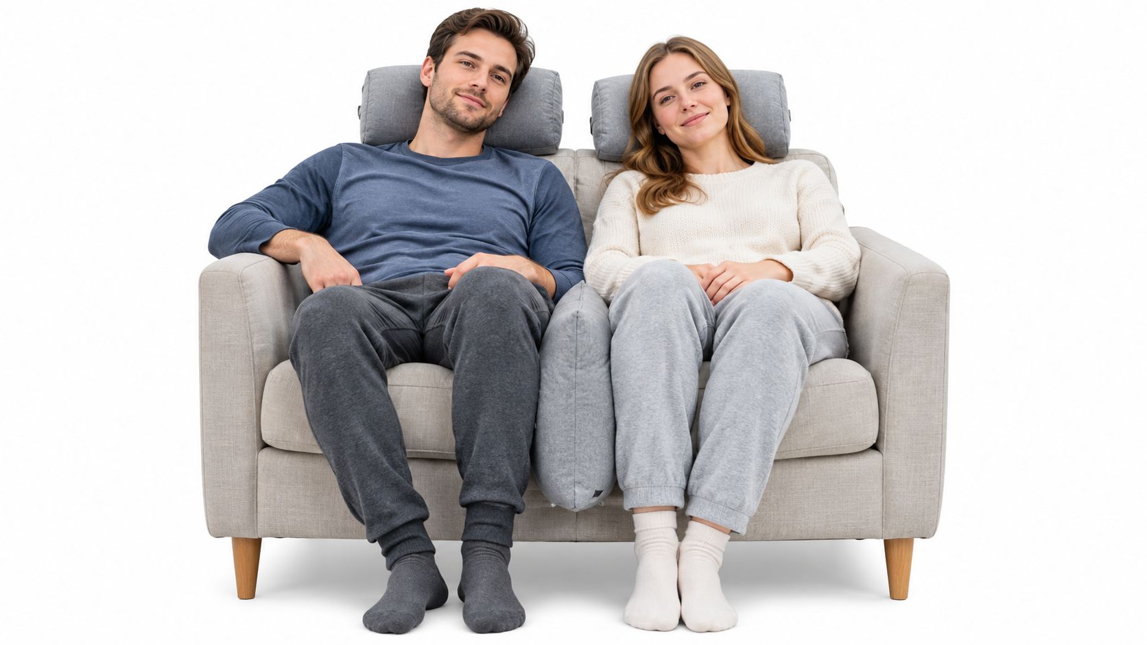 A young couple sits comfortably on a light-colored sofa with a large divider pillow between them.