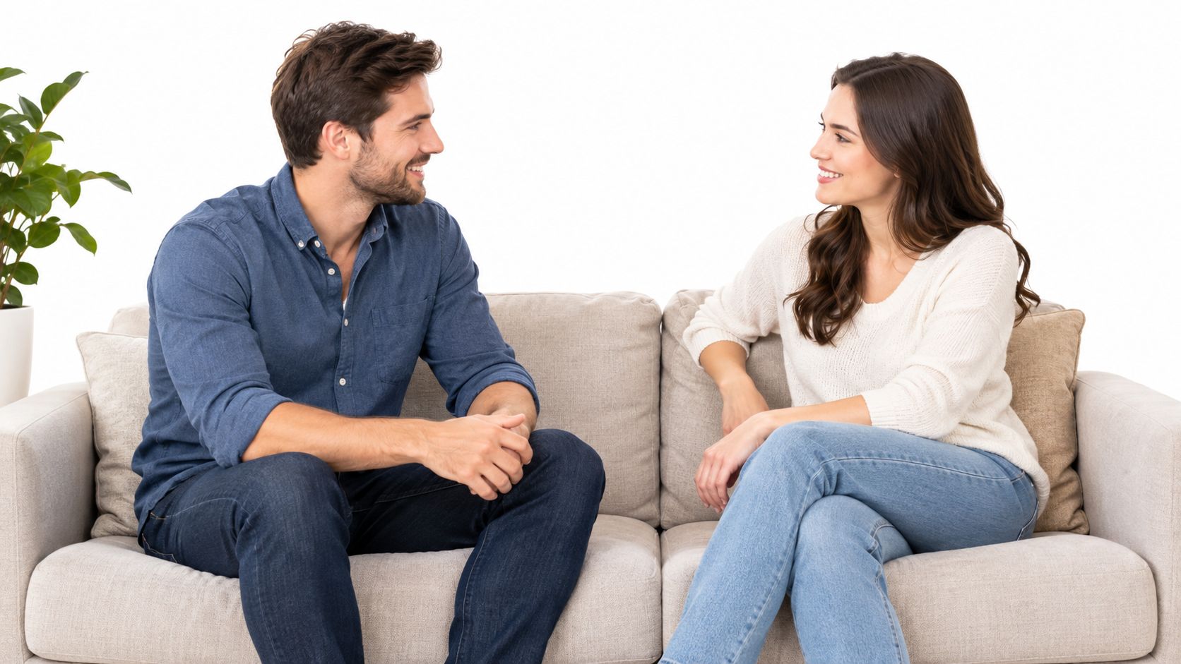 A smiling young couple sitting on a beige couch and having a friendly conversation together.