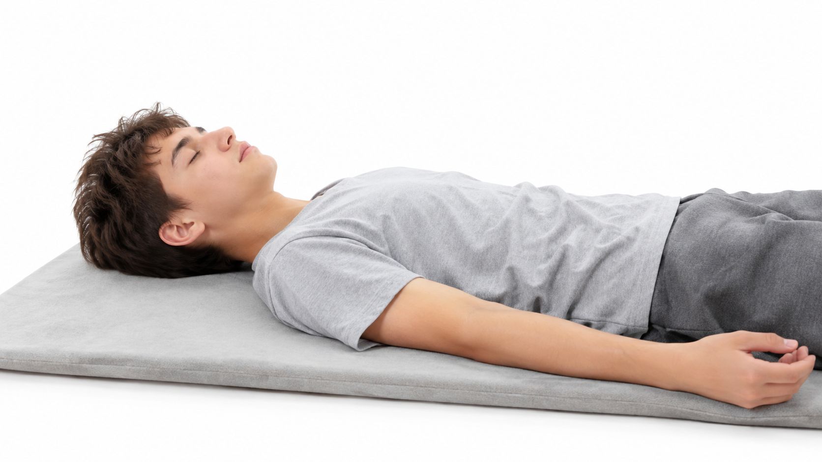 A teenager lying flat on his back on a gray mat, practicing relaxation or grounding techniques.