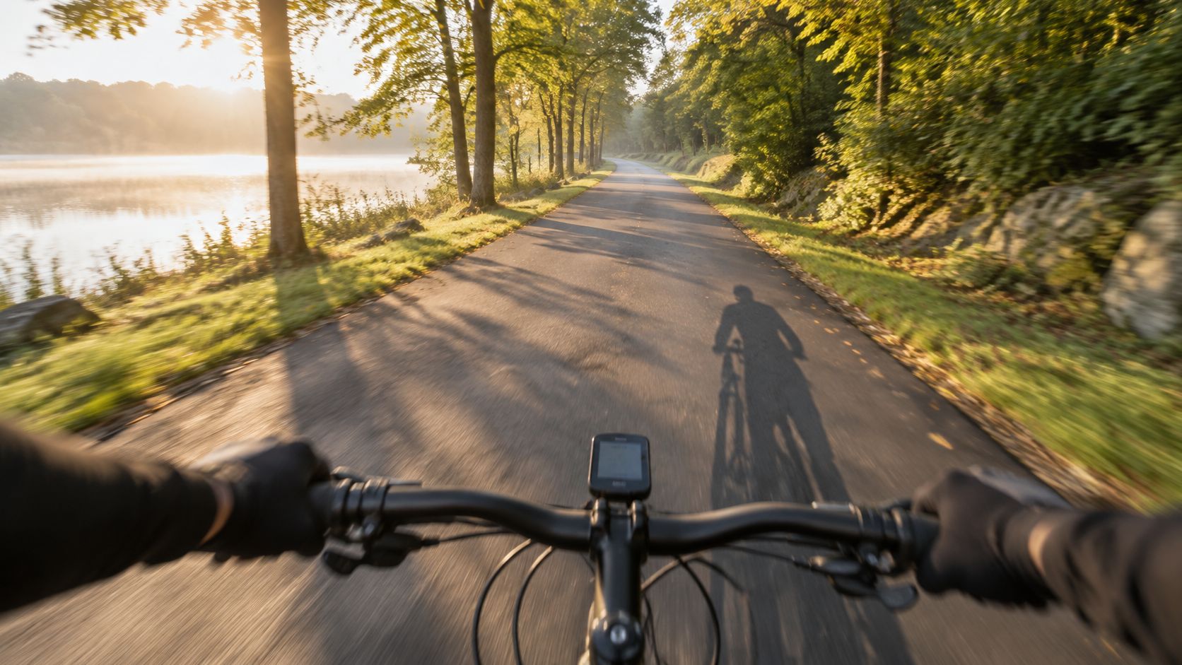 A first-person perspective view of a cyclist riding a bike on a scenic road at sunrise.