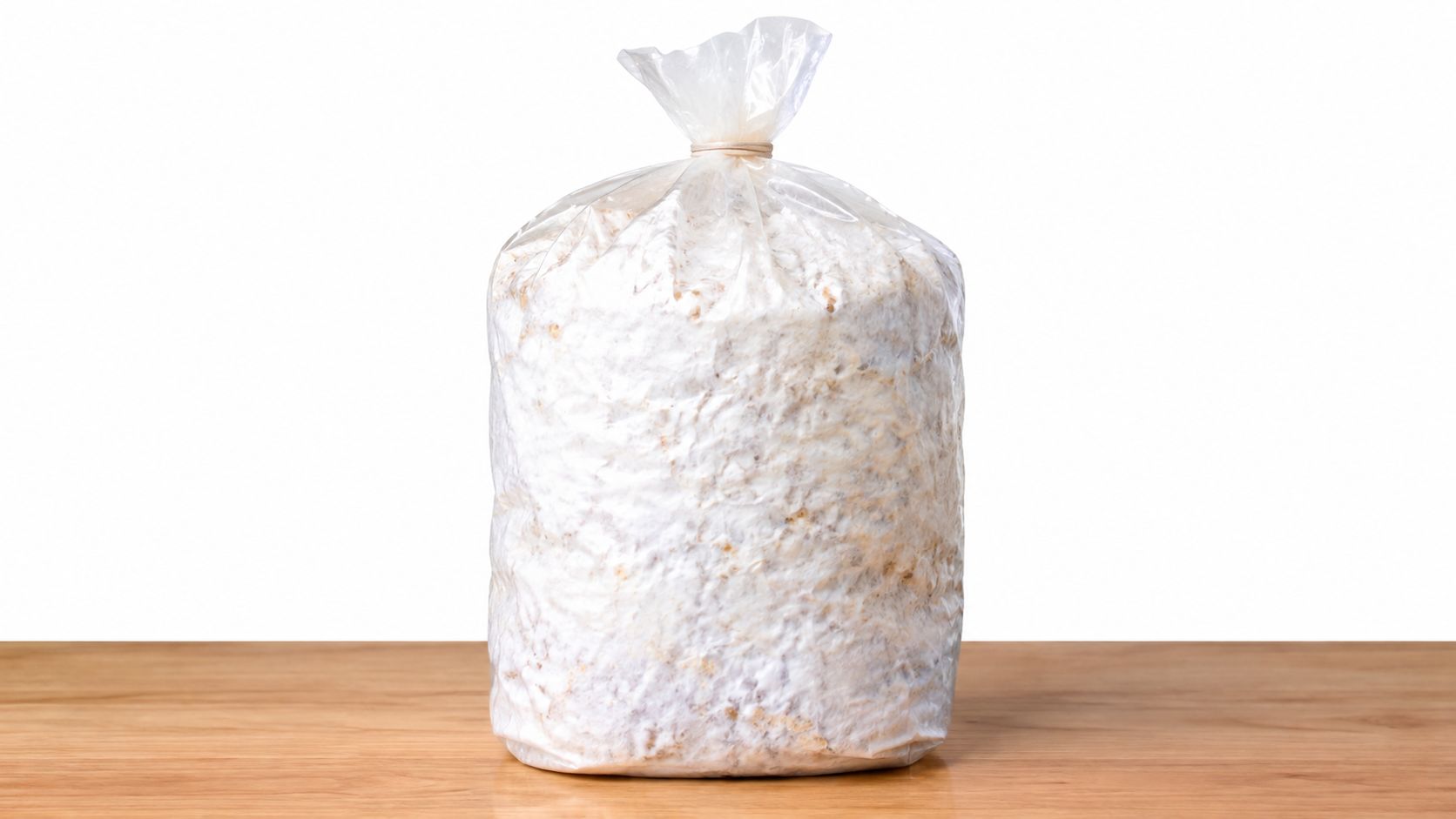 A fully colonized mushroom mycelium grow bag sitting on a wooden table against a white background.