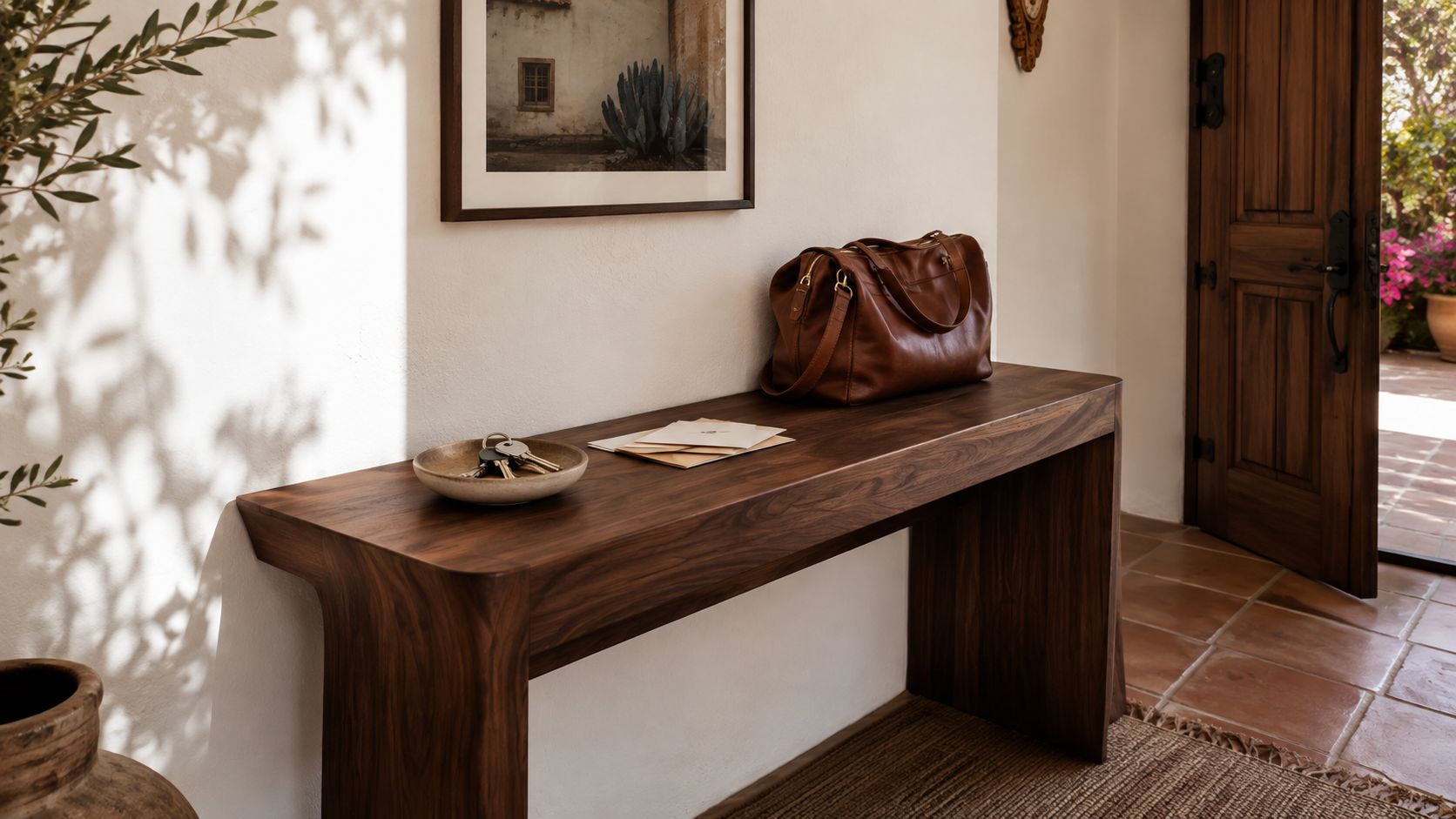 Consola de madera rústica en una entrada iluminada con un bolso de cuero, llaves y cartas encima.