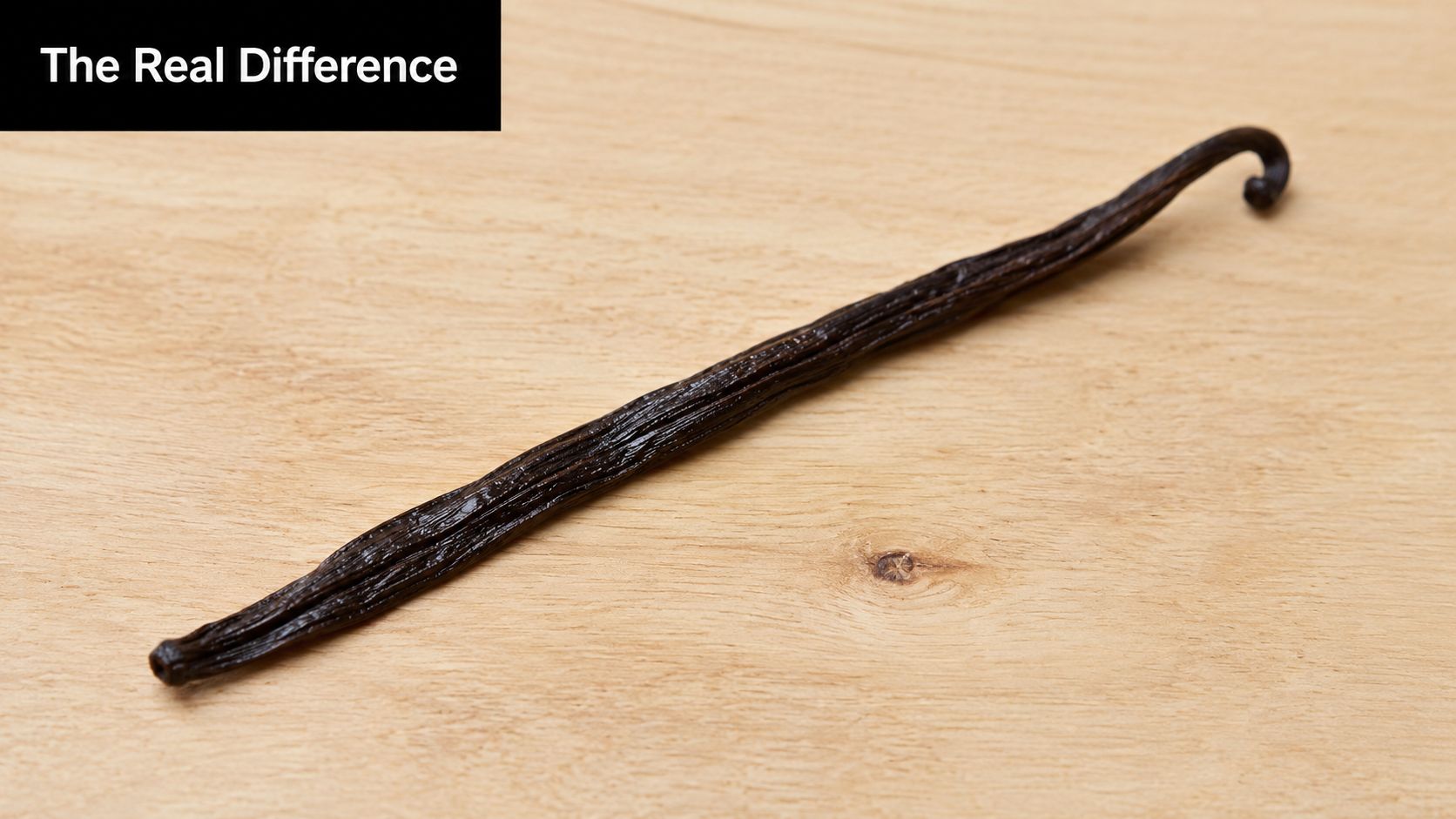 A single dried dark brown vanilla bean resting on a light textured wooden surface.