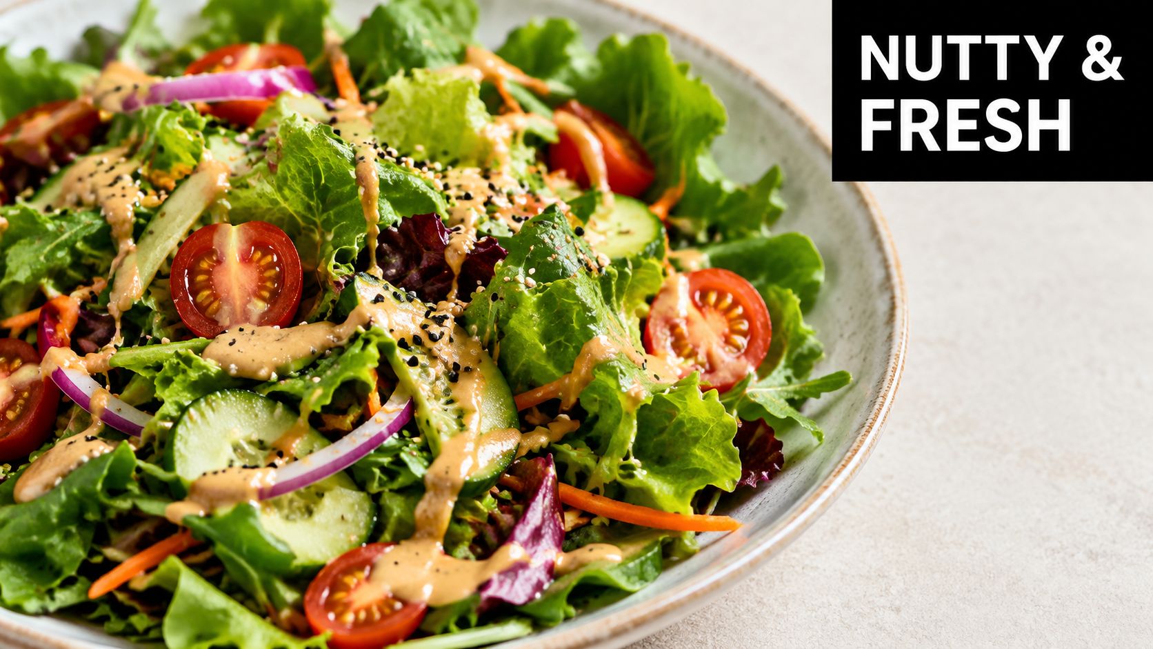 A fresh green salad in a white bowl drizzled with a creamy roasted sesame salad dressing.
