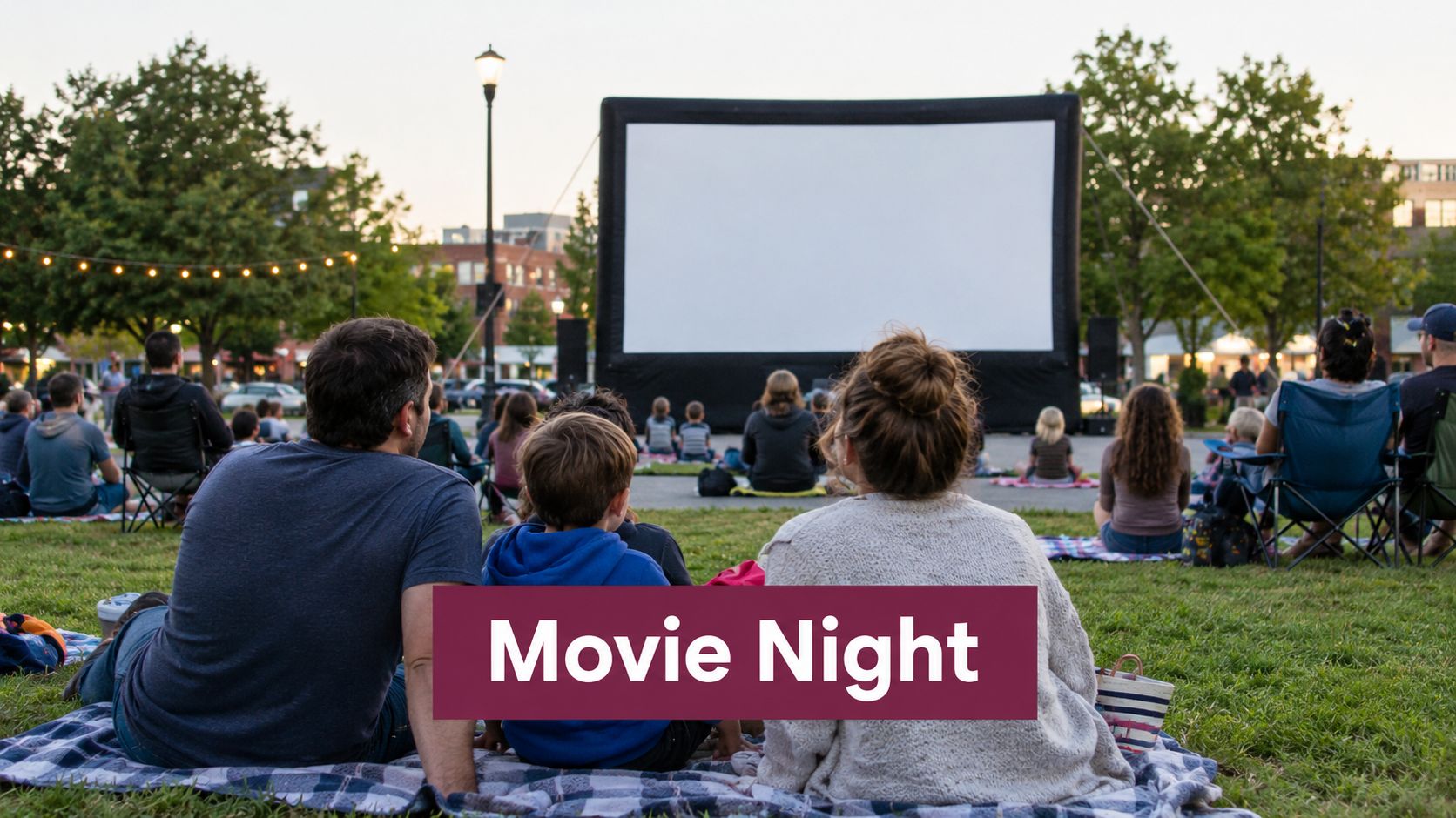 A family sitting on a blanket on the grass watching a movie at an outdoor cinema event.